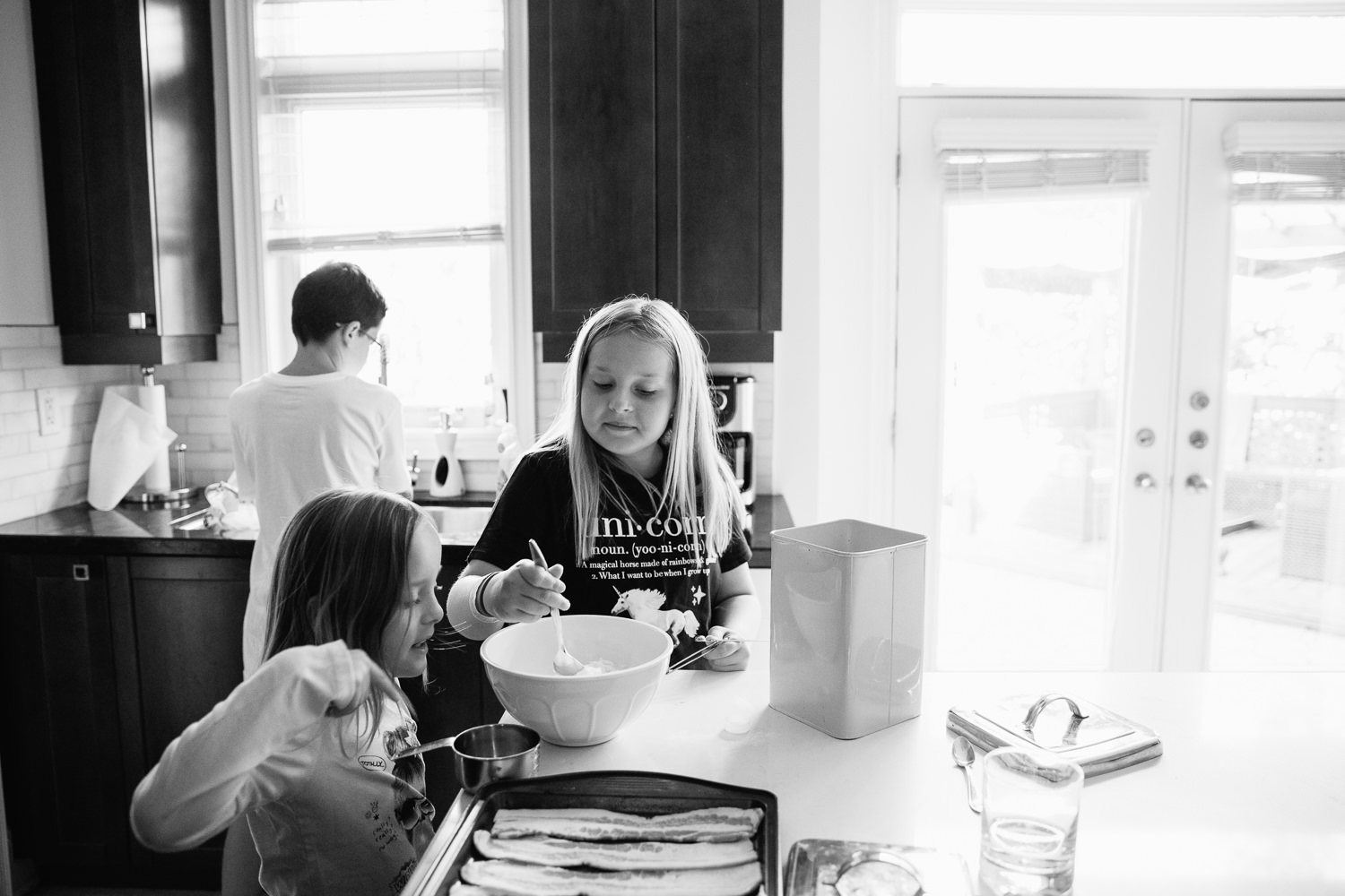 8 and 10 year old sisters standing at kitchen island mixing pancake batter for family brunch, 13 year old brother at sink behind them - Stouffville Lifestyle Photography