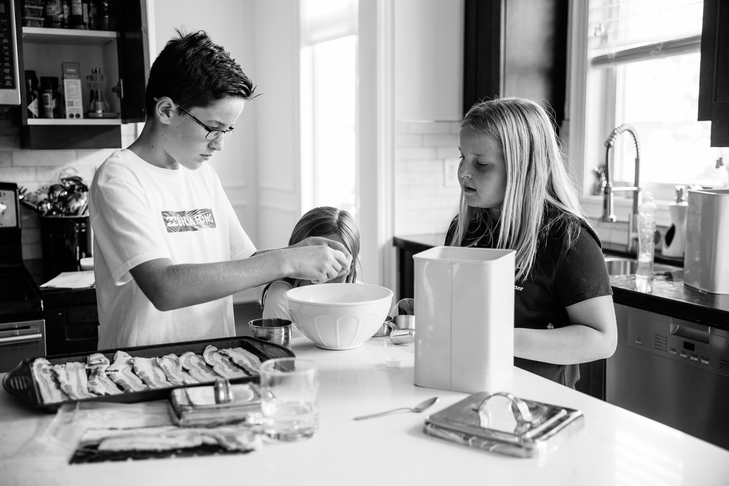 3 children standing at kitchen island mixing pancake batter for family brunch, 8 and 10 year old girls, 13 year old boy cracking eggs - Newmarket Lifestyle Photography