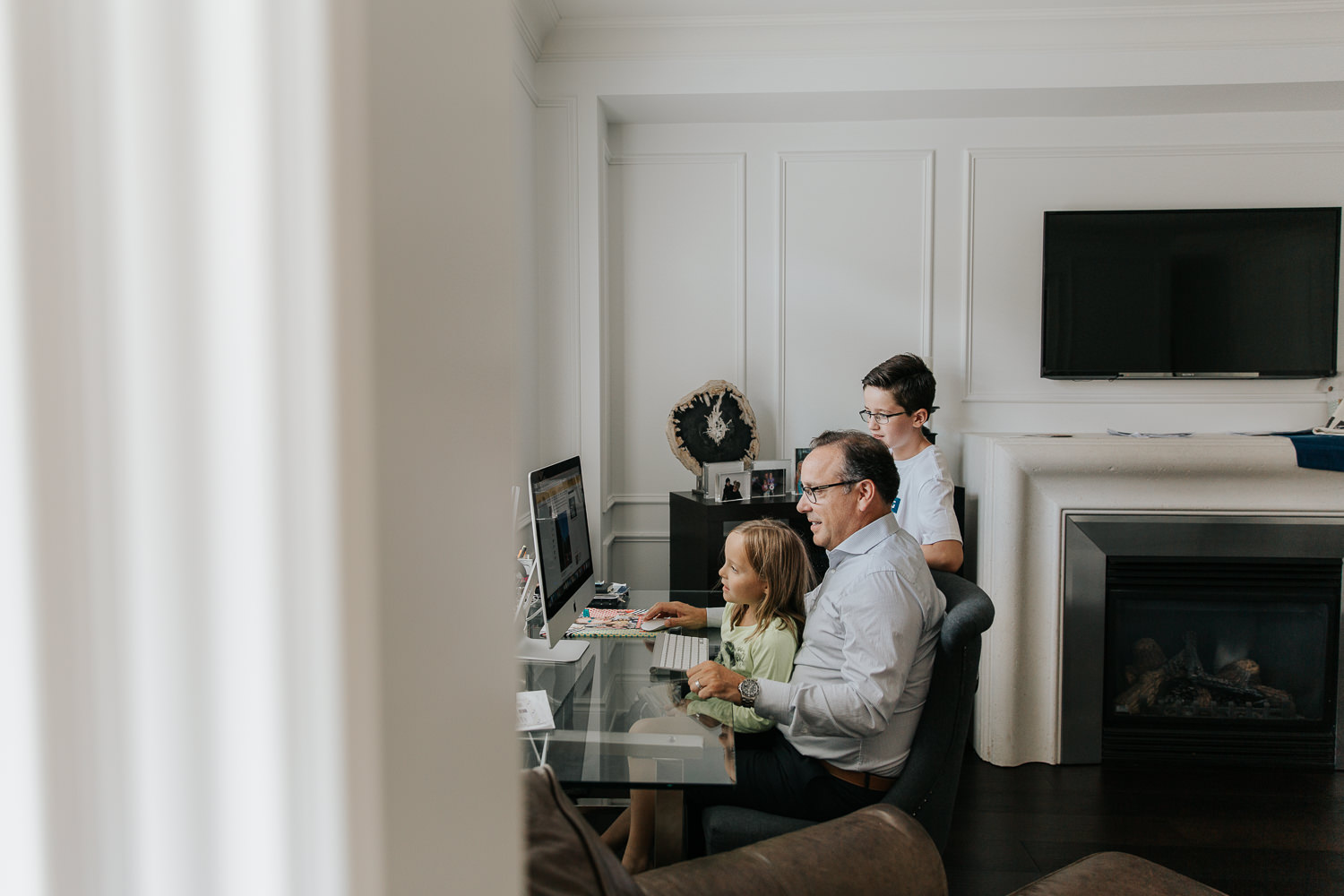 father sitting at desk with 8 year old daughter sitting in lap, 13 year old standing next to him, looking at computer - Newmarket In-Home Photography