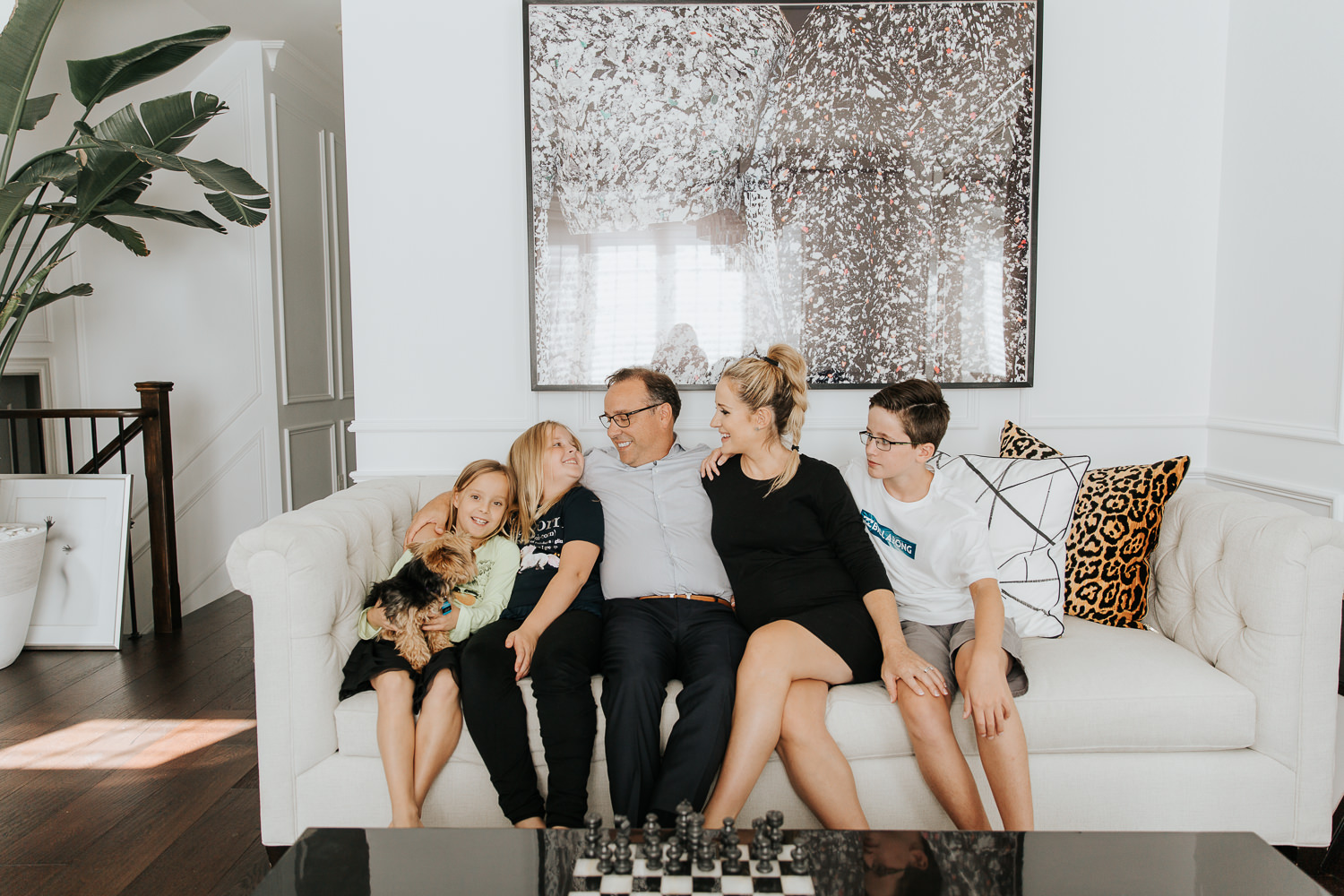 family of 5 sitting on couch together, smiling at one another, 2 daughters 1 son, 8 year old girl holding yorkie dog in lap - York Region In-Home Photography