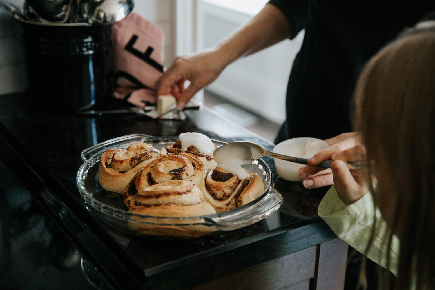 8 year old girl putting icing on cooked cinnamon buns for family brunch with help from mom - GTA In-Home Photos