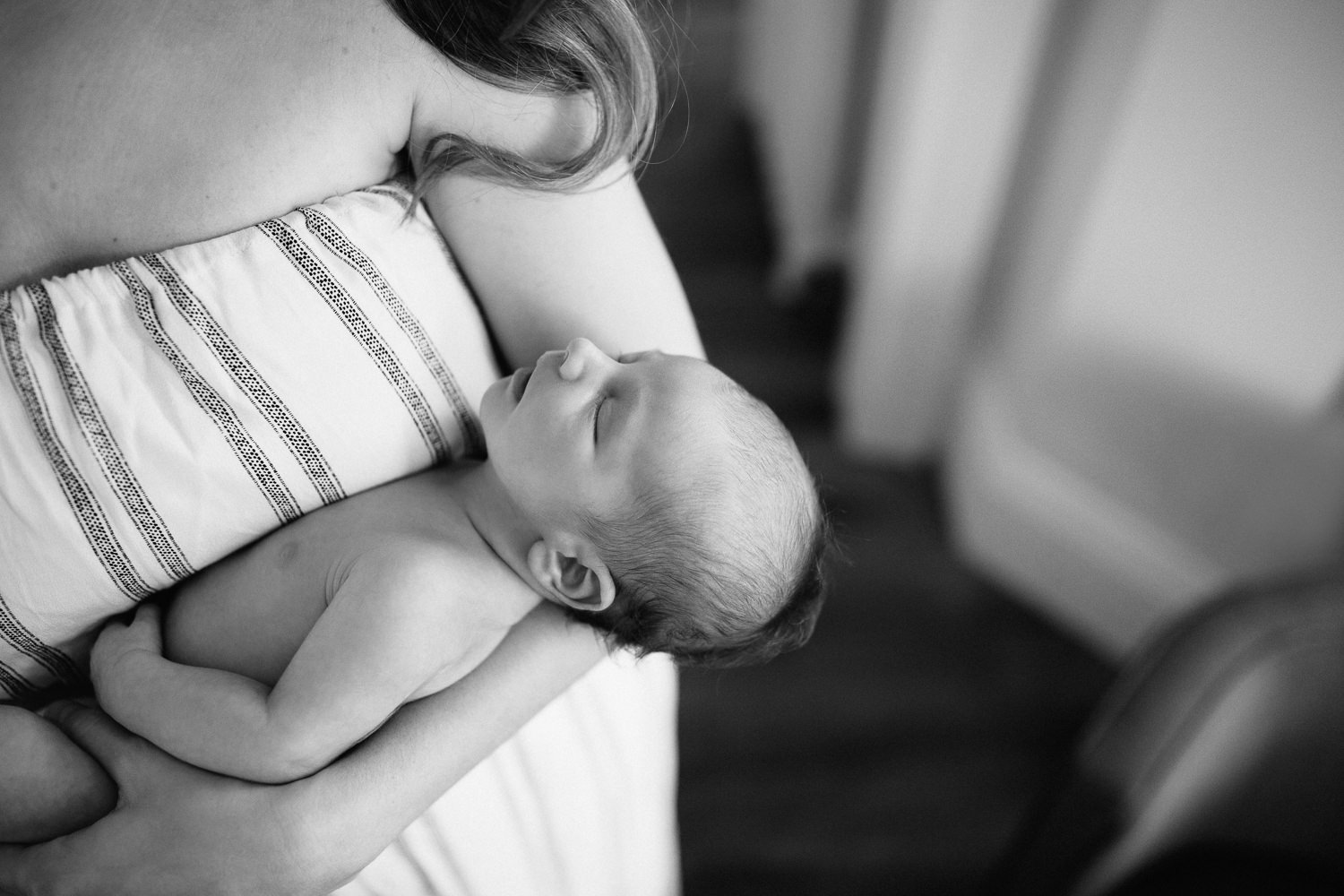 new mom with long dark hair wearing sleeveless striped romper standing and holding 2 week old baby boy in diaper -​​​​​​​ Markham In-Home Photography