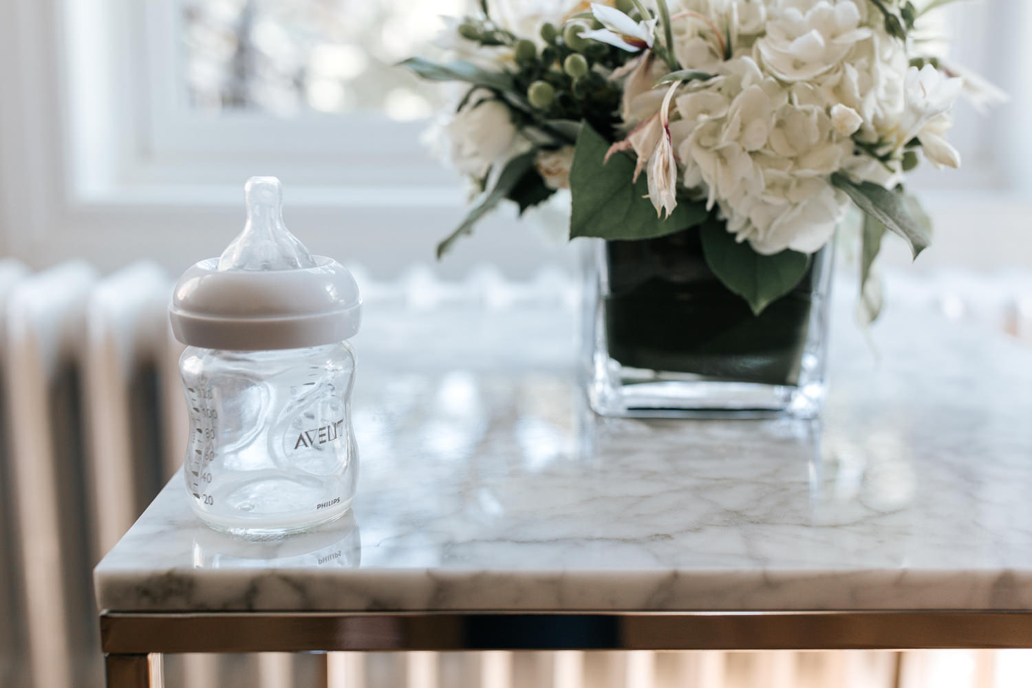clear glass baby bottle sitting on marble topped table next to neutral flower arrangement - York Region Lifestyle Photography
