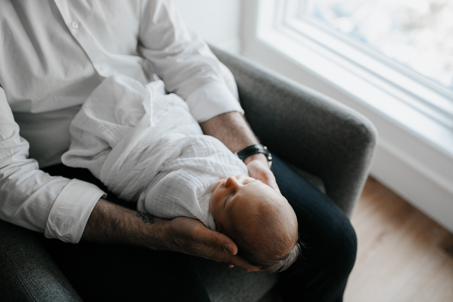 new dad sitting in nursery rocking chair, holding sleeping 2 week old baby boy in his arms - Stouffville Lifestyle Photography