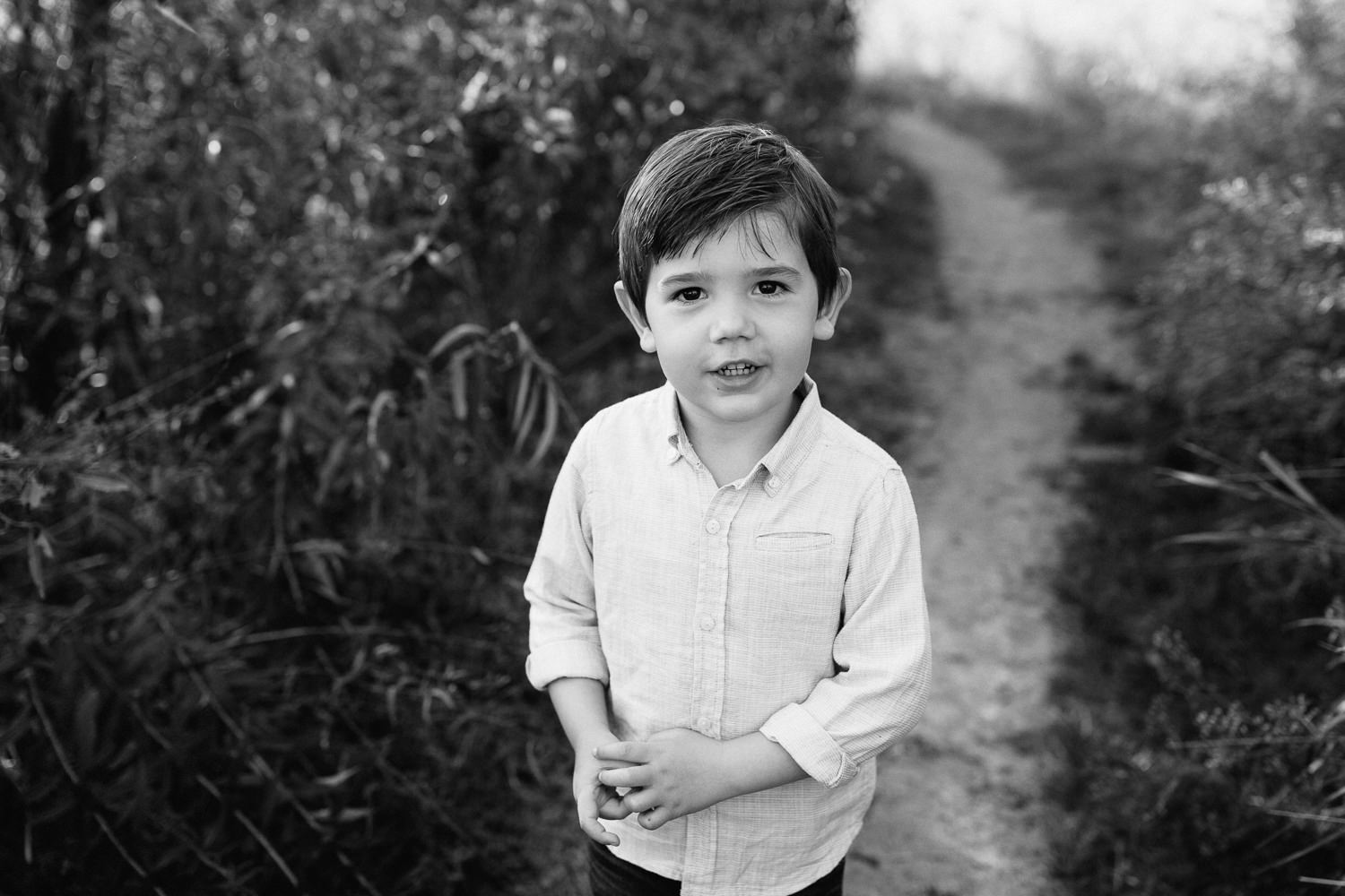 4 year old boy with dark hair and eyes wearing button down shirt standing on path looking up at camera - Markham In-Home Photos