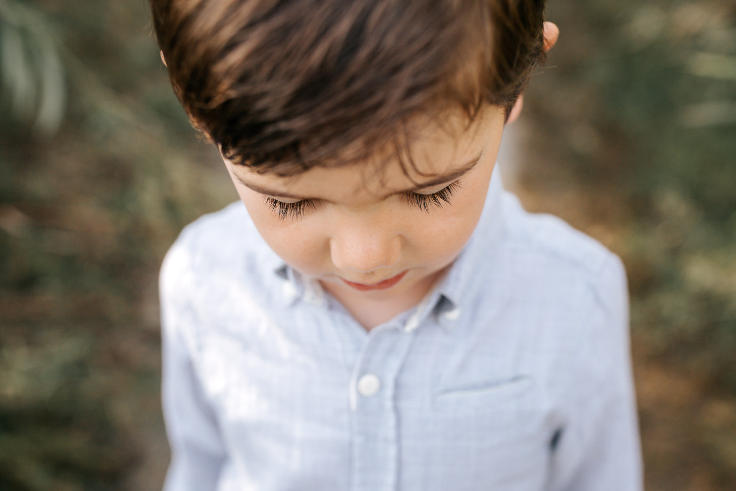 4 year old boy with dark hair and eyes wearing button down shirt standing on path looking down, close up of long eyelashes - Barrie In-Home Photos
