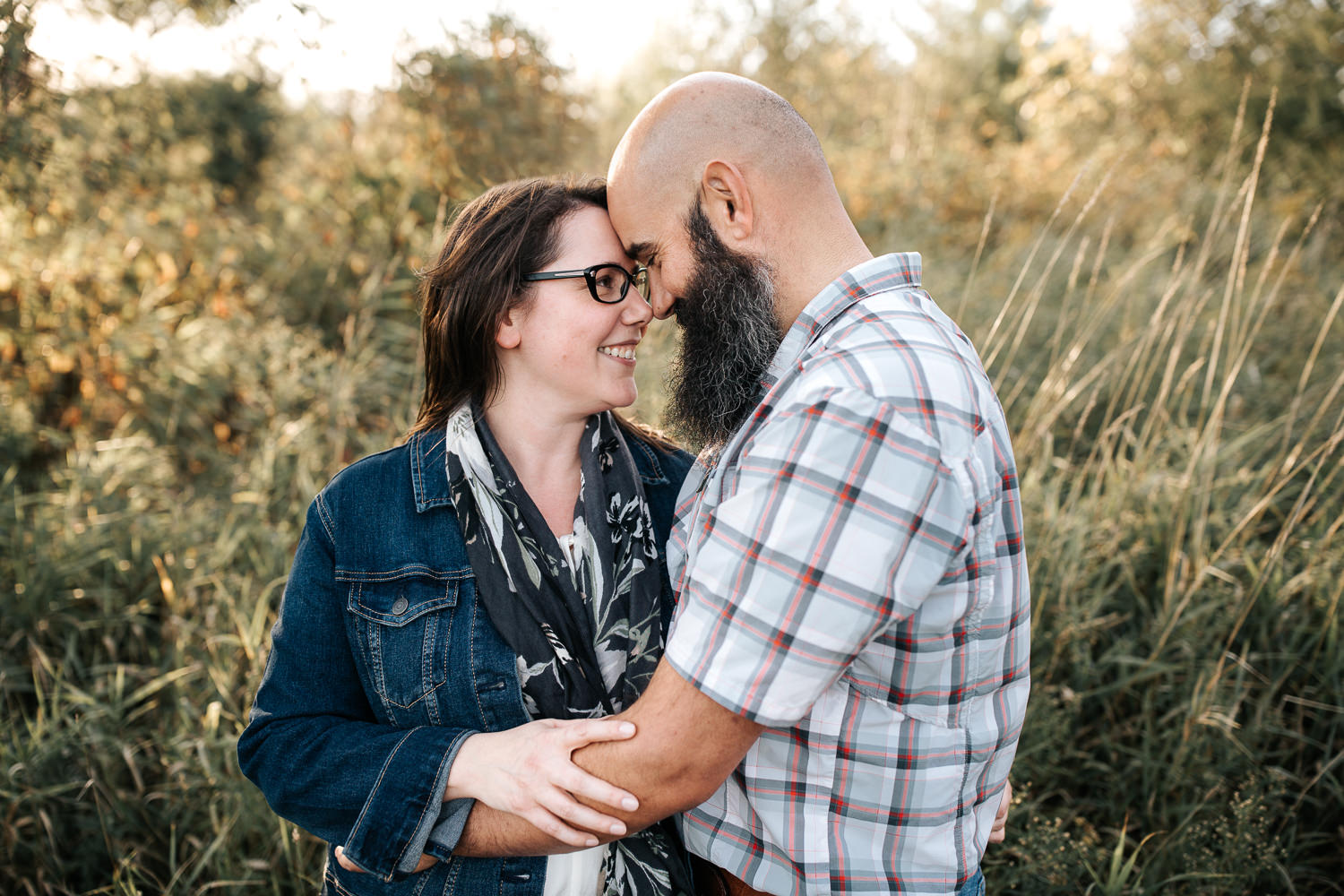 couple standing in grassy field at sunset, husband's arms around wife's waist, her hand on his arm, foreheads touching - Markham Lifestyle Photos