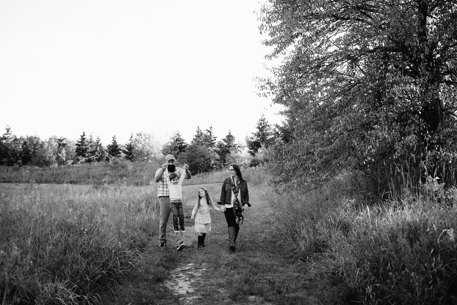 family of 4 holding hands, walking down path in grassy field, dad swinging son by both arms, mother and daughter smiling at them - GTA Lifestyle Photos