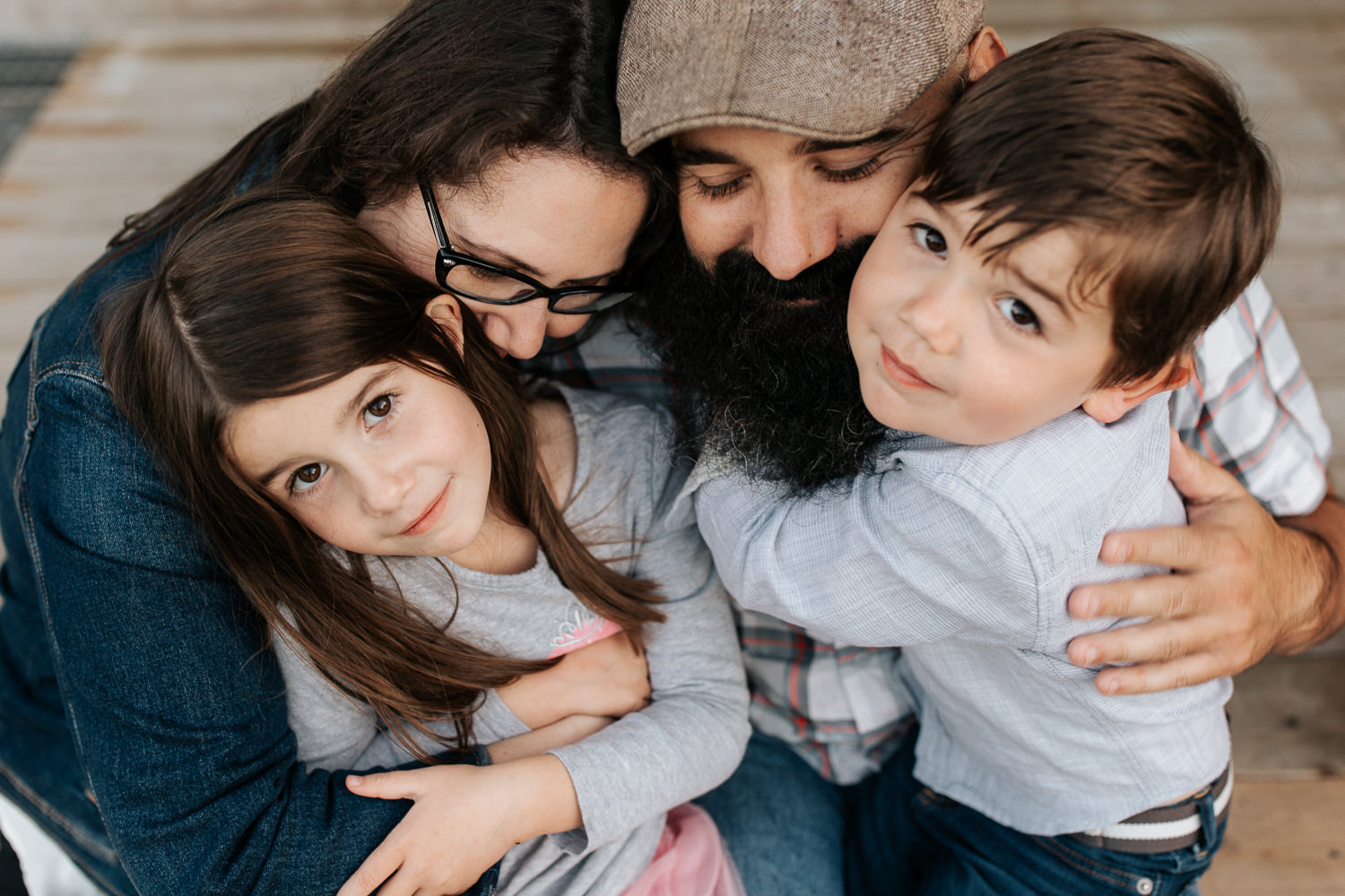 family of four sitting on porch, 4 year boy sitting in dad's lap and 5 year old girl in mom's, snuggled up together in an family hug, son and daughter looking up at camera - Newmarket Lifestyle Photos