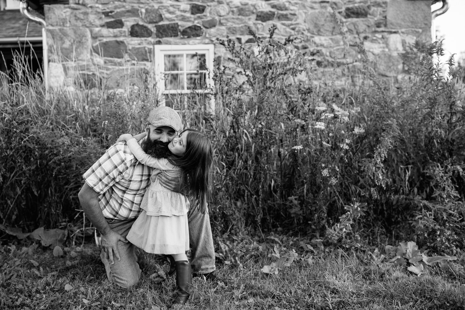 father bending down on one knee in front of old stone house as 5 year old girl hugs him around the neck, dad's arm around daughter - Stouffville Lifestyle Photos