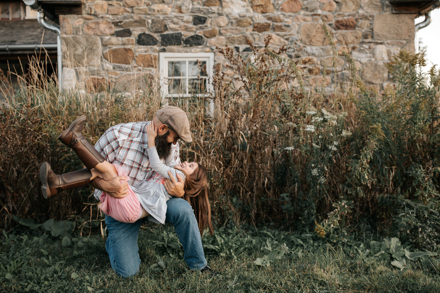 father bending down on one knee in front of old stone house, 5 year old girl swept up in his arms, daughter's hand around dad's neck - GTA Lifestyle Photos