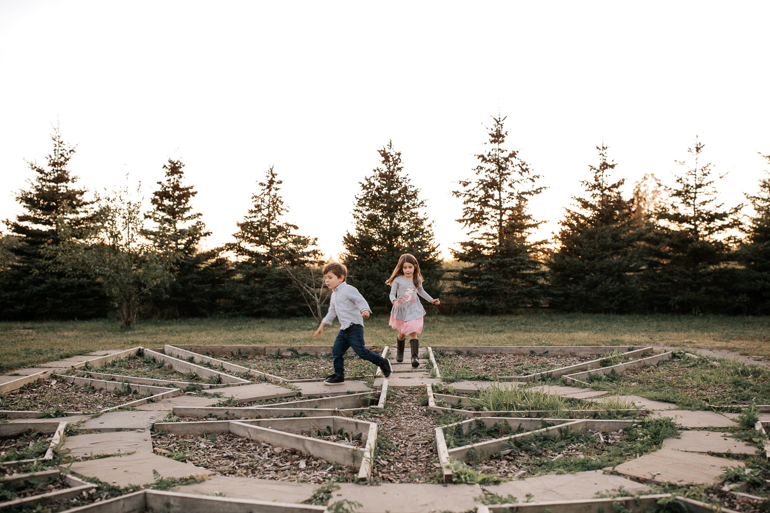 4 year old boy and 5 year old girl both with dark hair running through maze on ground as sun sets behind them - York Region Lifestyle Photos