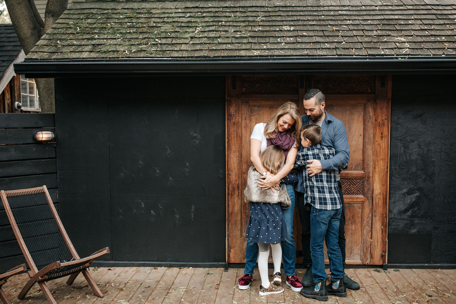 family of 4 standing on front of dark home with old doors, 7 year old girl hugging mother, 9 year old boy hugging father - Barrie Lifestyle Photography