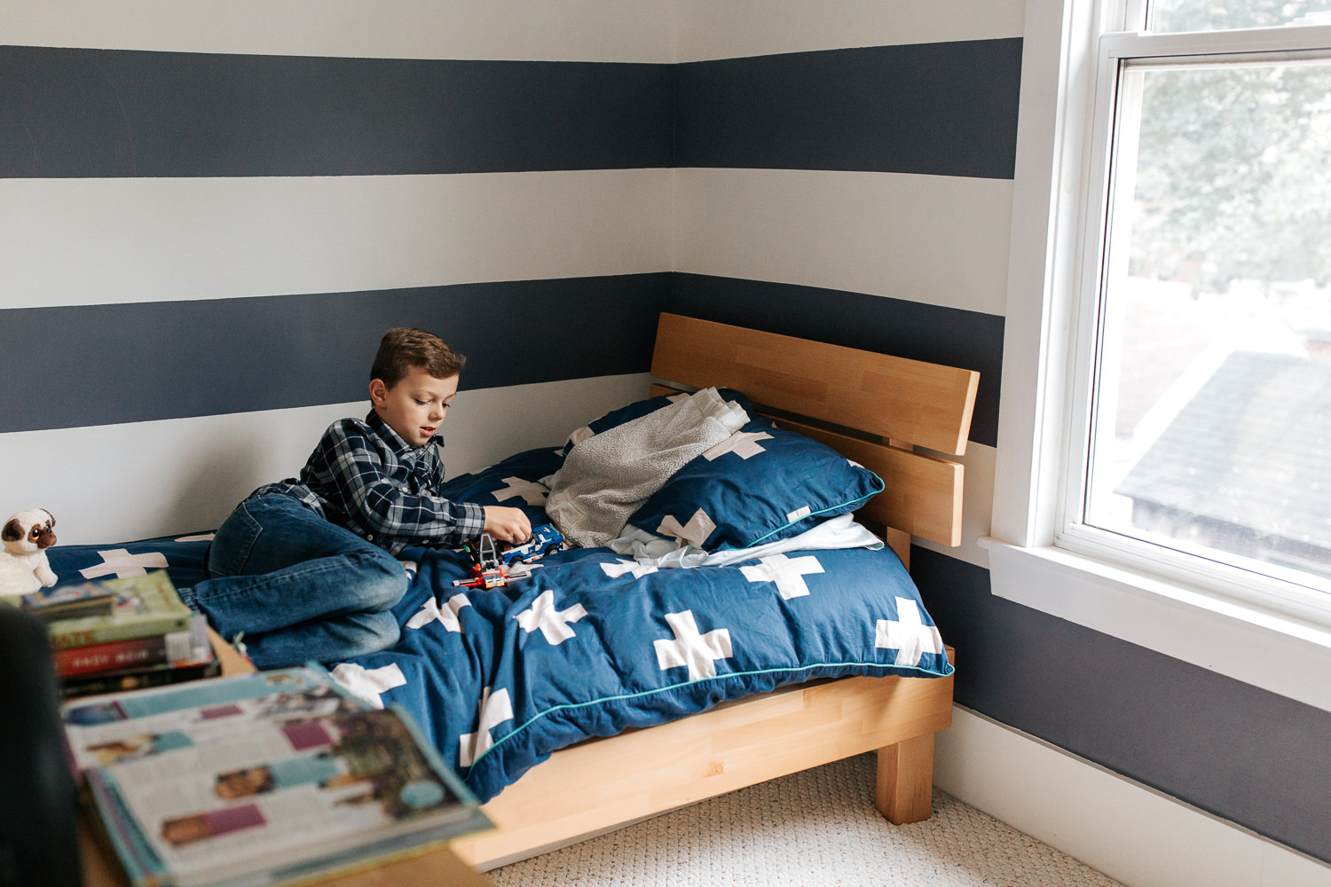 9 year old boy in plaid shirt with light brown hair lying on bed in blue and white room playing with lego - Barrie In-Home Photography