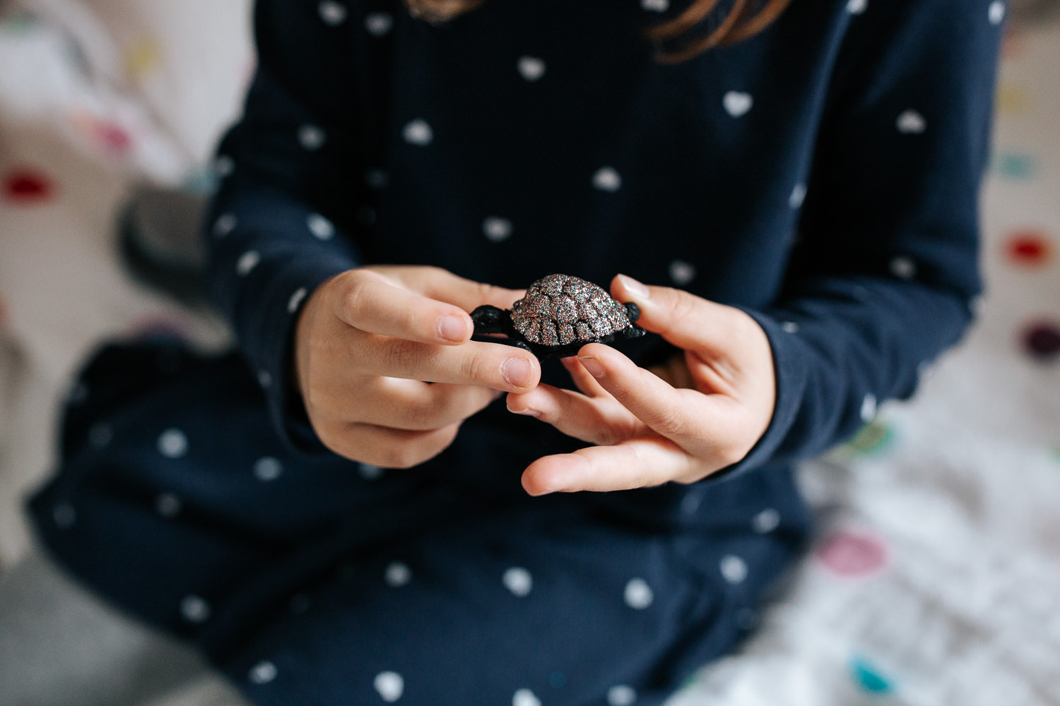 7 year old girl in polka dot dress sitting on bed in her room, holding sparkly turtle toy, close up of hands - Newmarket In-Home Photos