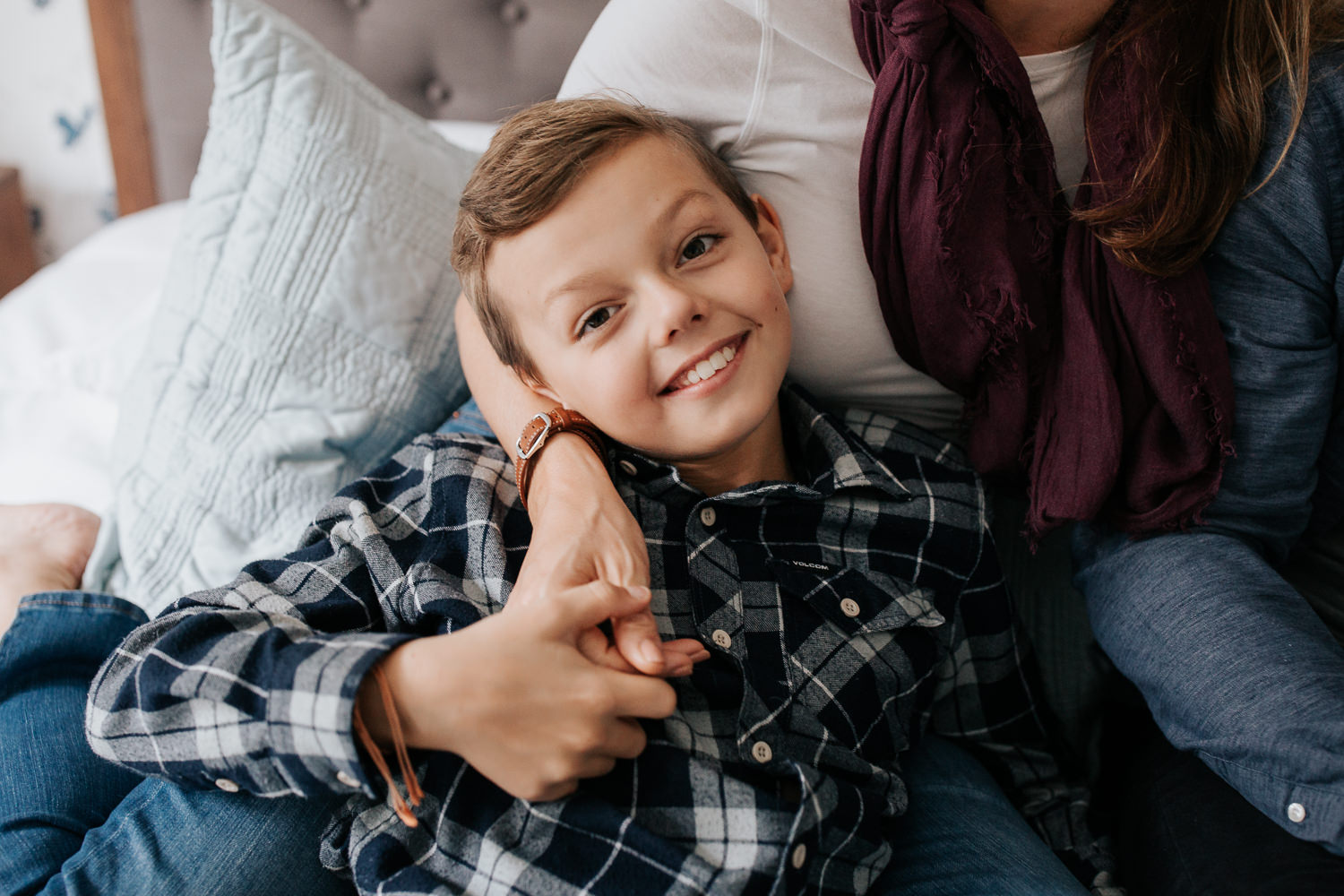 9 year old boy lying in mom's lap as they sit on bed, looking up and smiling at camera - Stouffville Lifestyle Photography