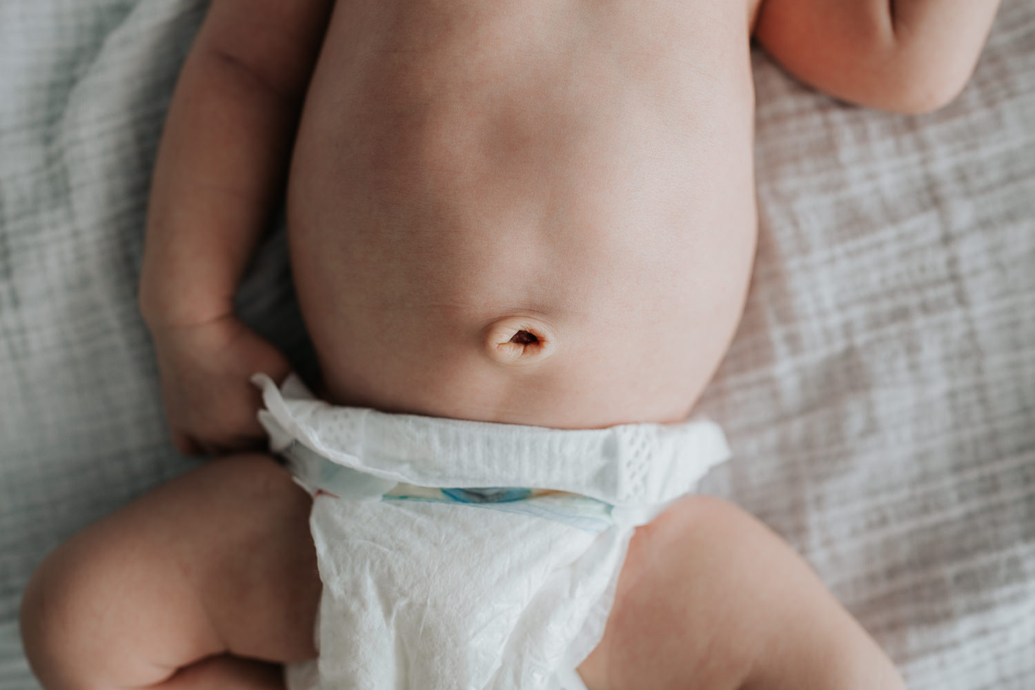 2 week old baby boy in diaper lying on white bed, close up of bellybutton - Uxbridge Lifestyle Photography