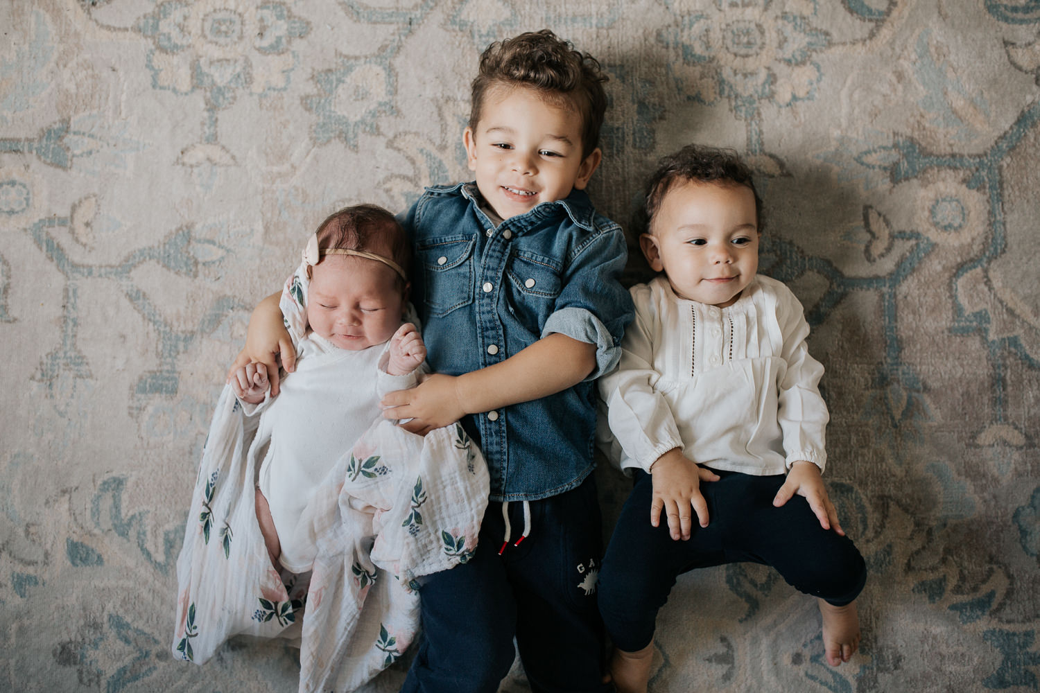 3 siblings lying on floor, 2 week old baby girl held by 2 year old big brother, 1 year old toddler sister next to boy - Stouffville In-Home Photos