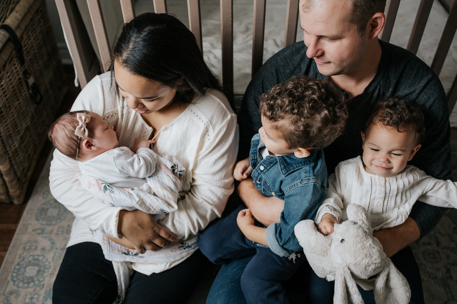 family of 5 sitting on floor of nursery leaning against crib, mom holding 2 week old baby girl, dad snuggling 2 year old boy and 1 year old daughter in his lap - York Region In-Home Photos