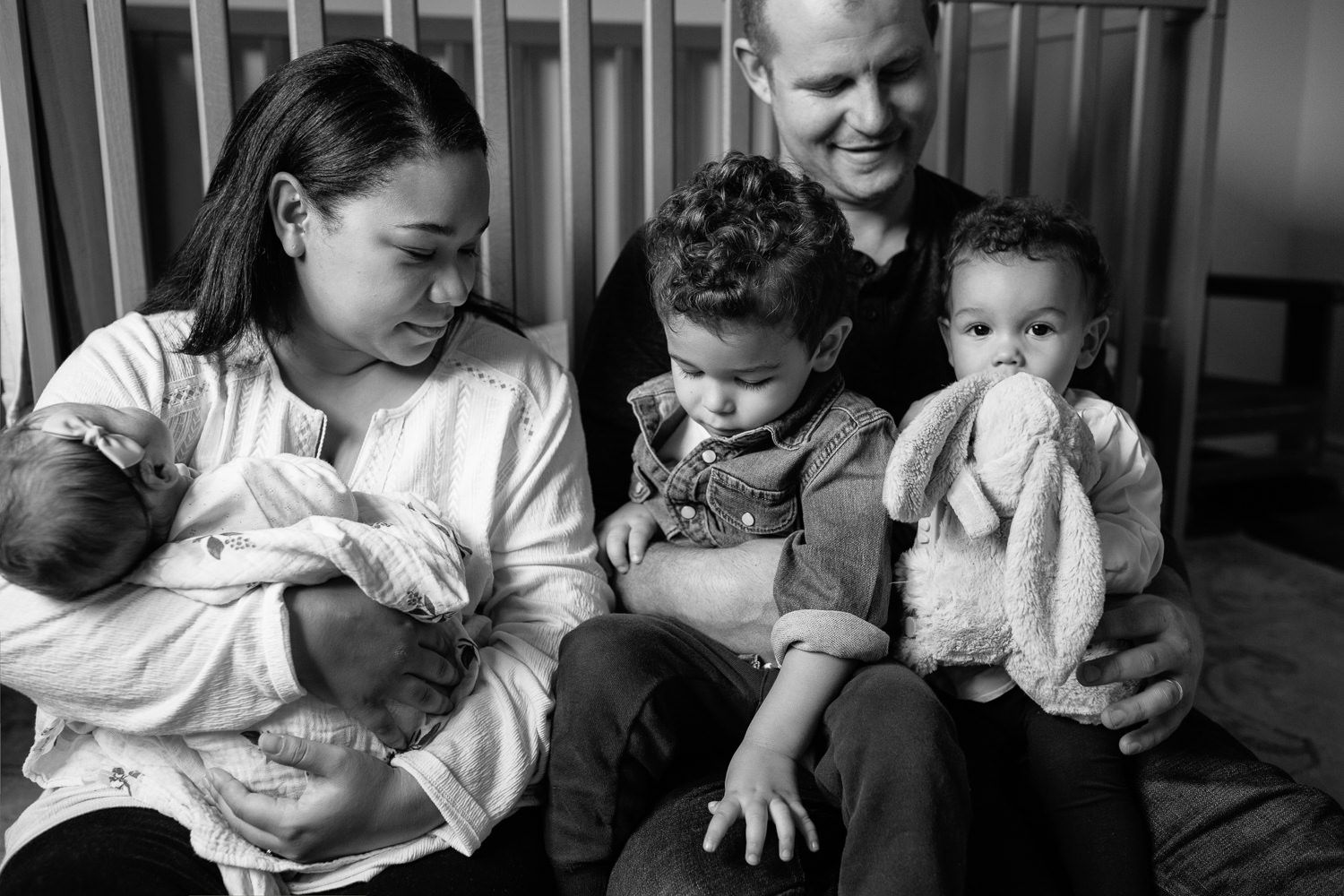 family of 5 sitting on floor of nursery leaning against crib, mom holding 2 week old baby girl, dad snuggling 2 year old boy and 1 year old daughter in his lap - Stouffville Lifestyle Photos