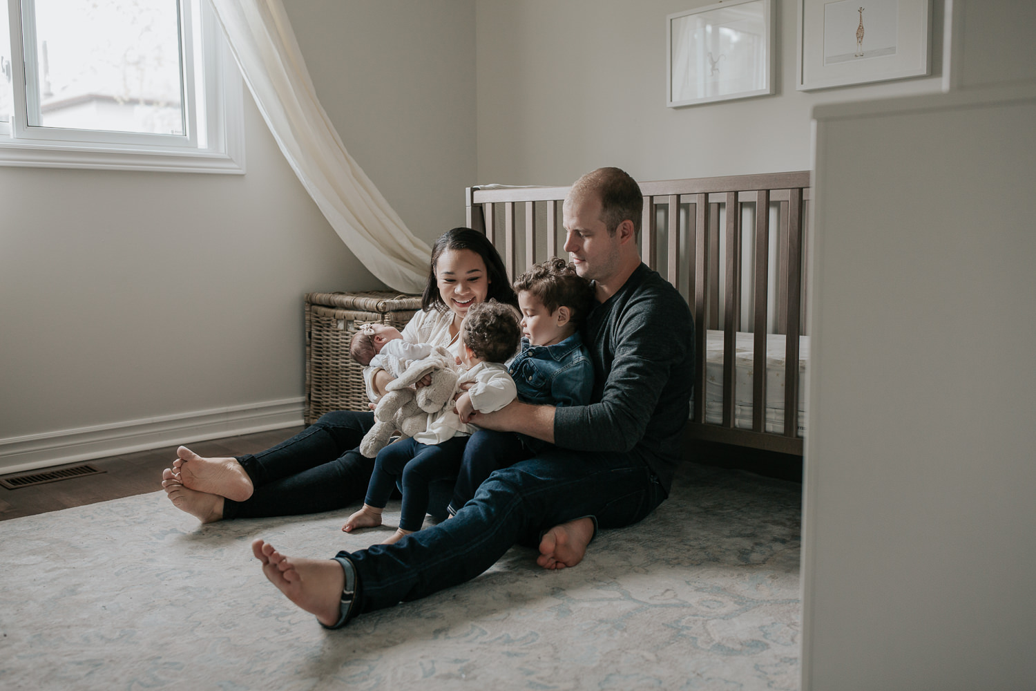 family of 5 sitting on floor of nursery leaning against crib, mom holding 2 week old baby girl, dad snuggling 2 year old boy and 1 year old daughter in his lap - Markham Lifestyle Photos