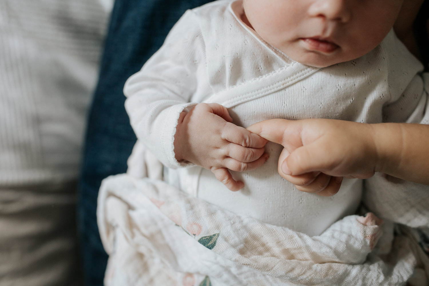 close up of 2 week old baby girl in white onesie and swaddle holding 2 year old big brother's finger - Markham In-Home Photos