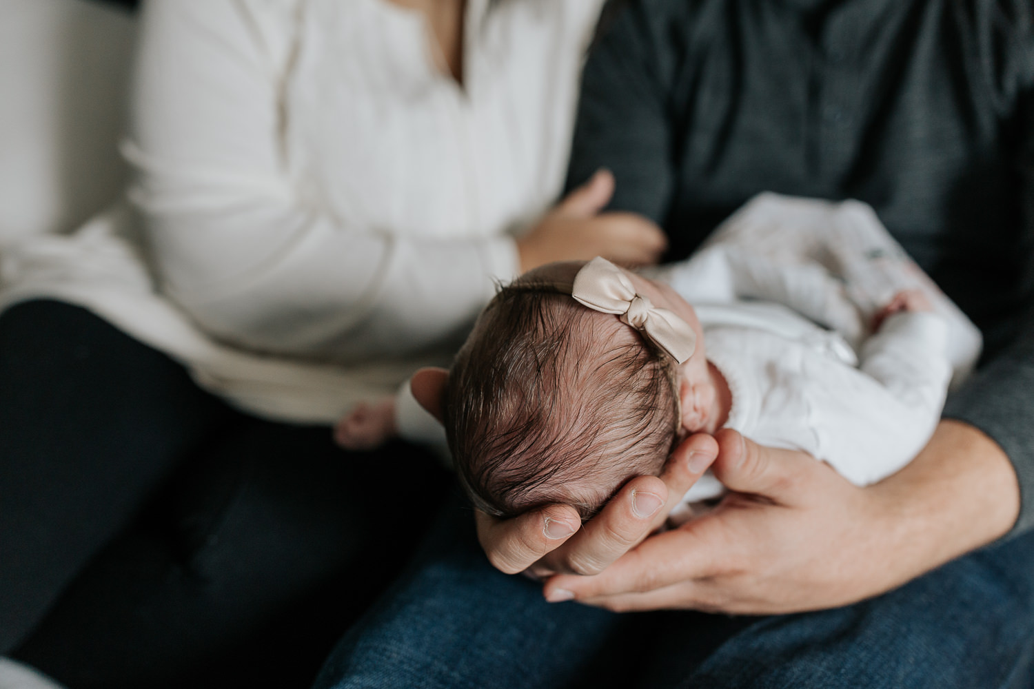 2 week old baby girl lying in dad's arms, her head in his hands, mom sitting beside them, close up of daughter's hair - Barrie In-Home Photos