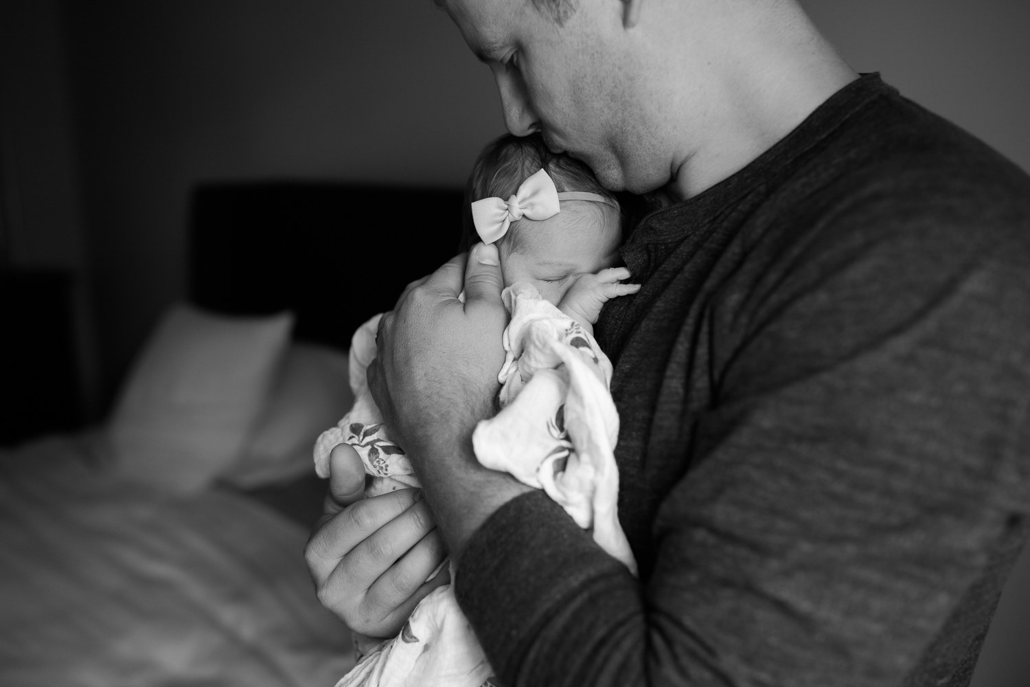 2 week old baby girl wrapped in swaddle sleeping on dad's chest, father kissing daughter on top of head - Newmarket Lifestyle Photos
