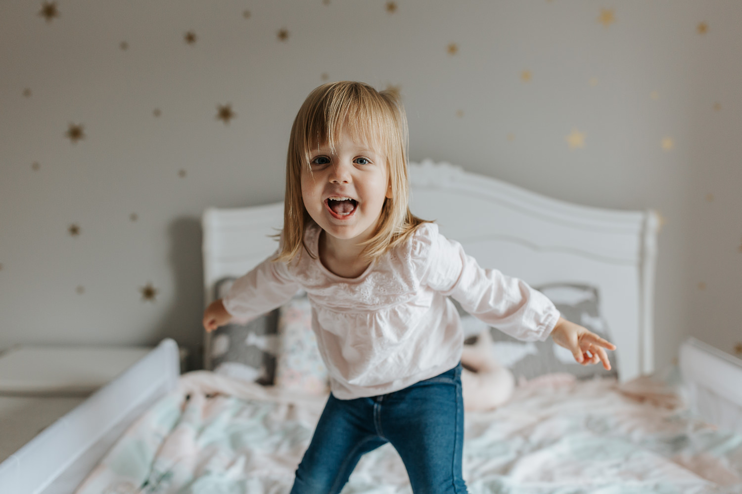 Stouffville In-Home Photography -blonde toddler girl jumping on bed with gold star decals on her wall, toddler bed, happy