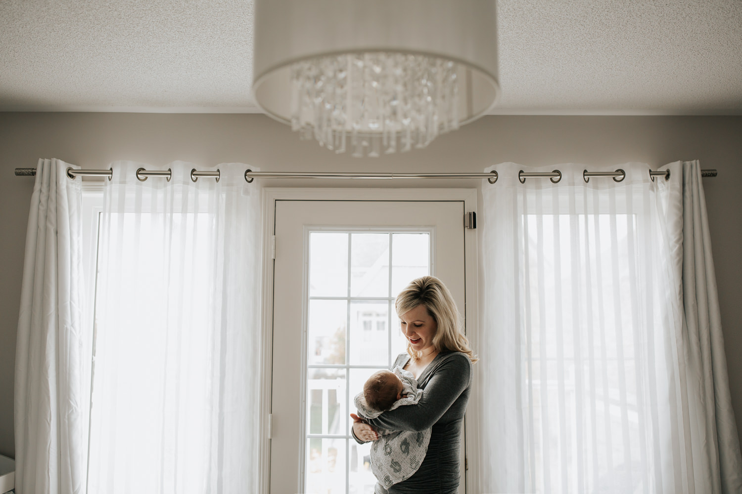 GTA In-Home Photos  - blonde mom adoring her new 2 week old baby boy standing by the door with a crystal chandelier up above