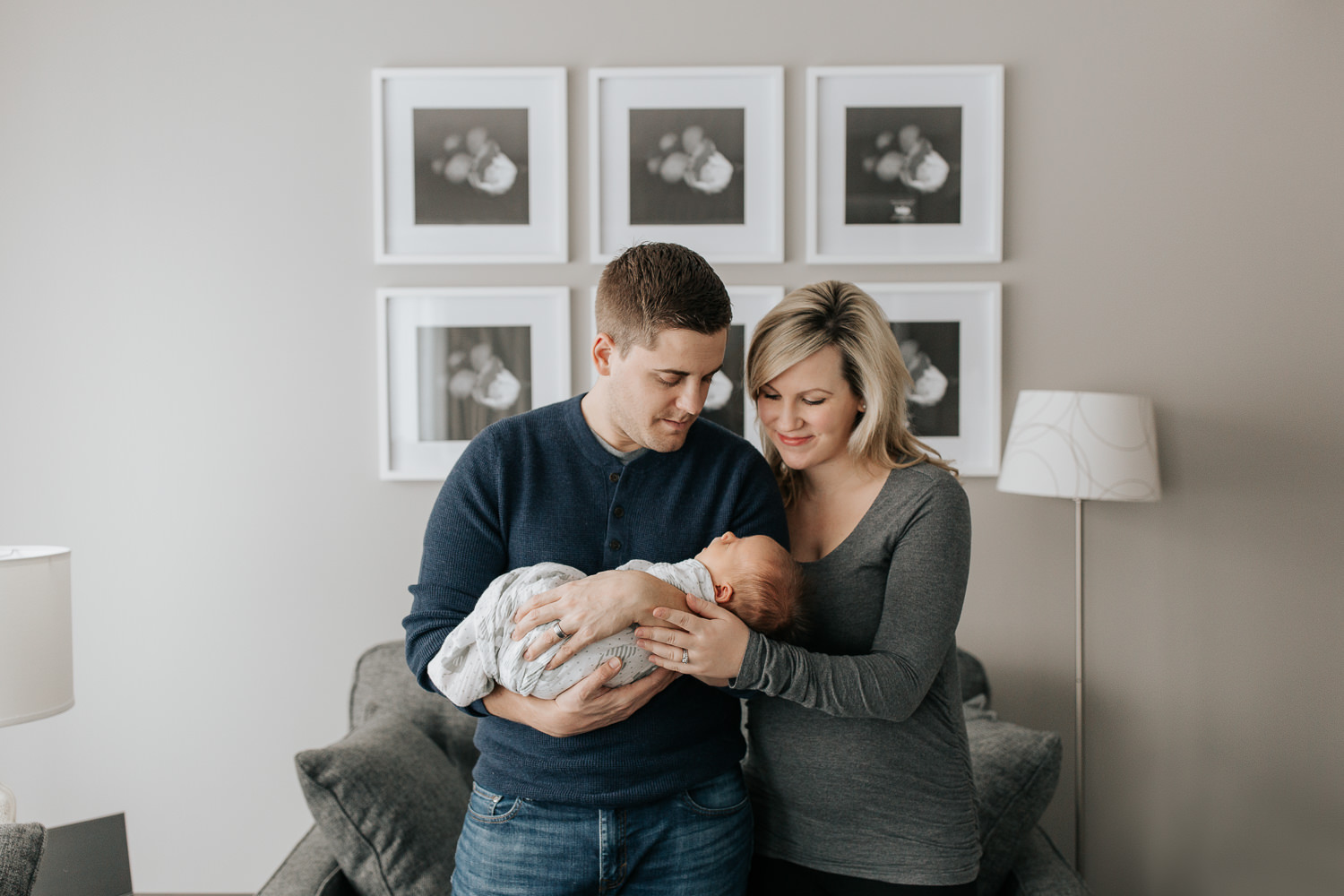 husband and wife standing in living room, father holding 2 week old baby boy in his arms, mom's hand on son - GTA Lifestyle Photography