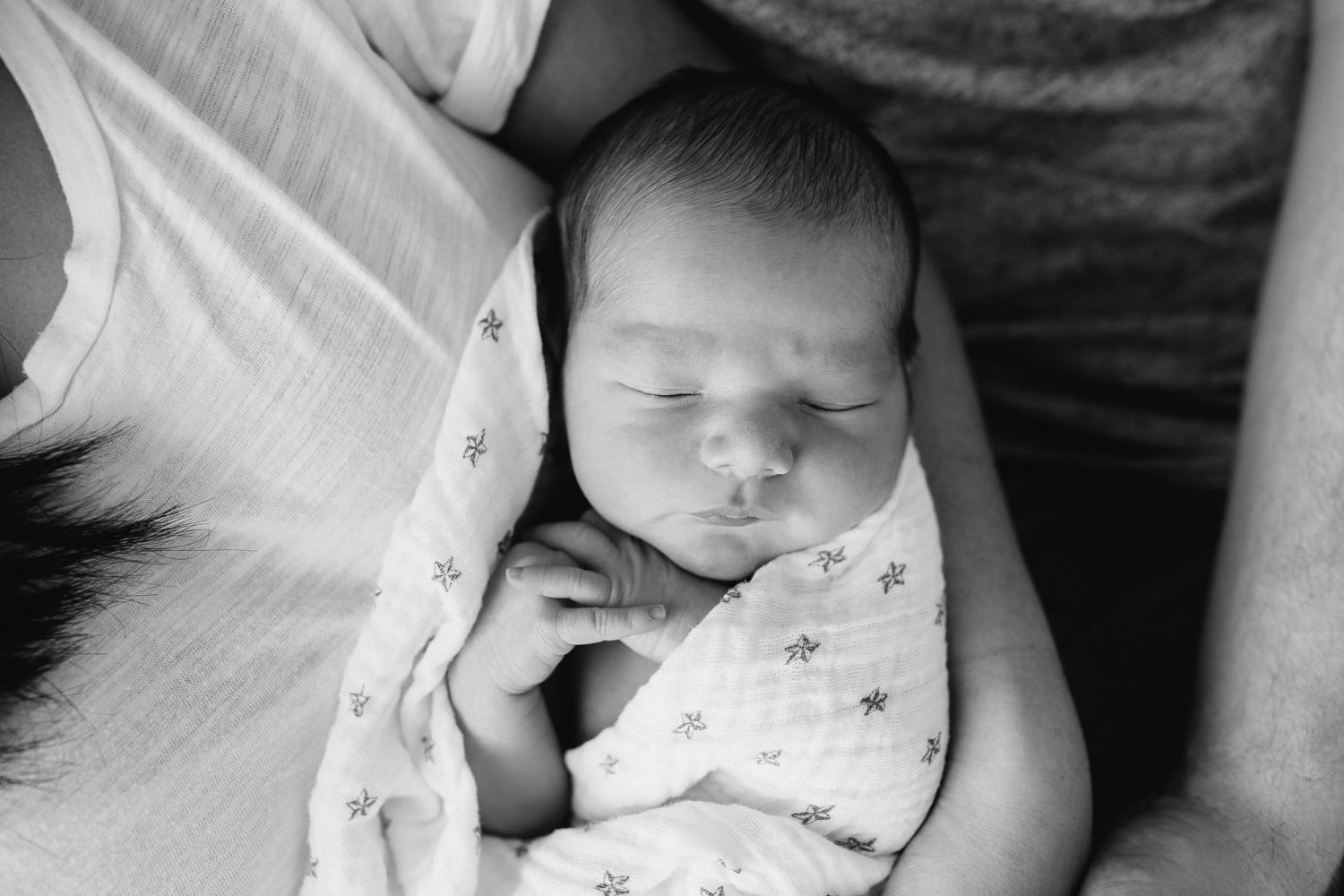 close up of 2 week old sleeping, swaddled baby boy with dark hair lying in his mom's arms, hands folded - Stouffville Lifestyle Photography