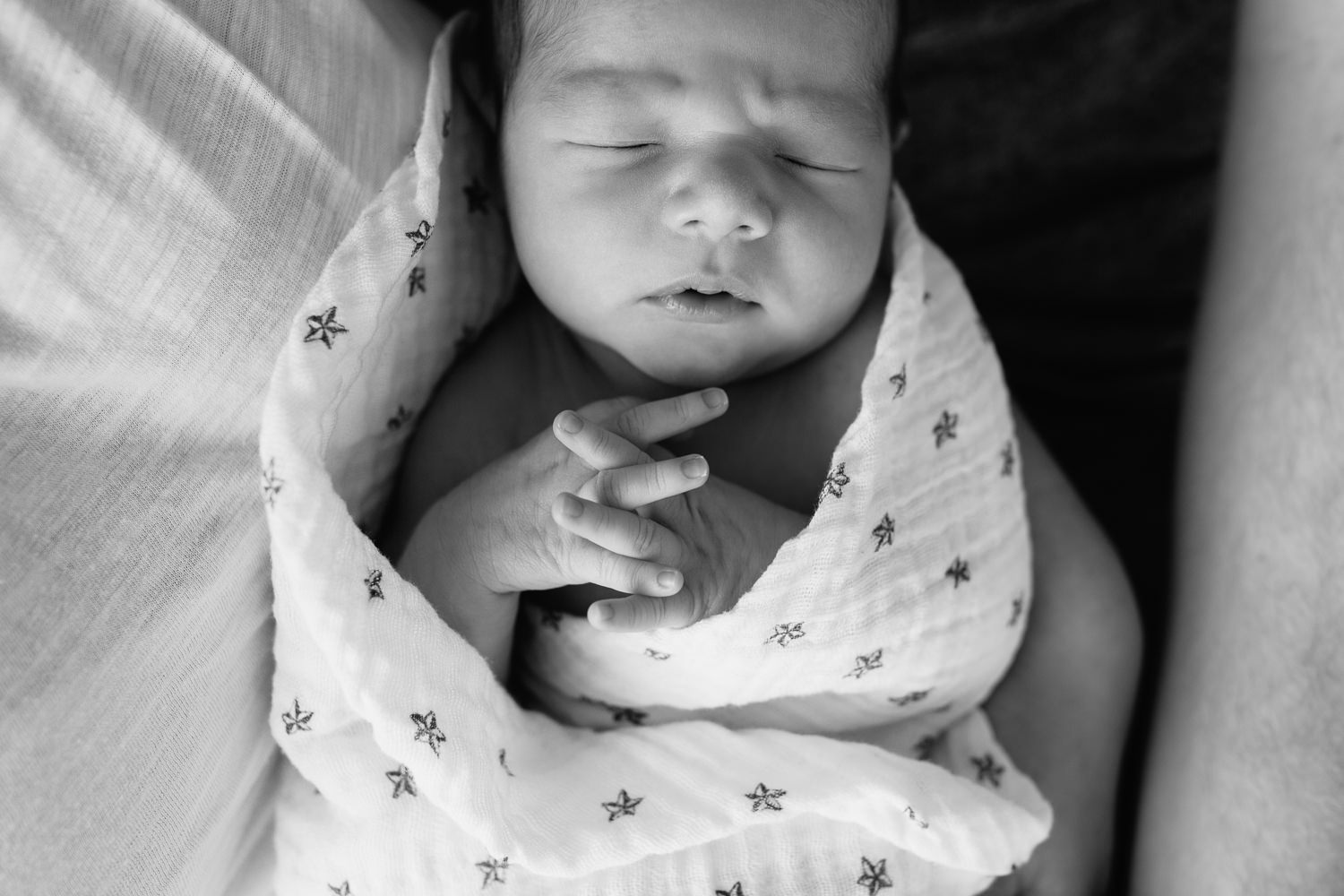 close up of 2 week old sleeping, swaddled baby boy with dark hair lying in his mom's arms, hands folded, fingers interlaced - Stouffville In-Home Photography