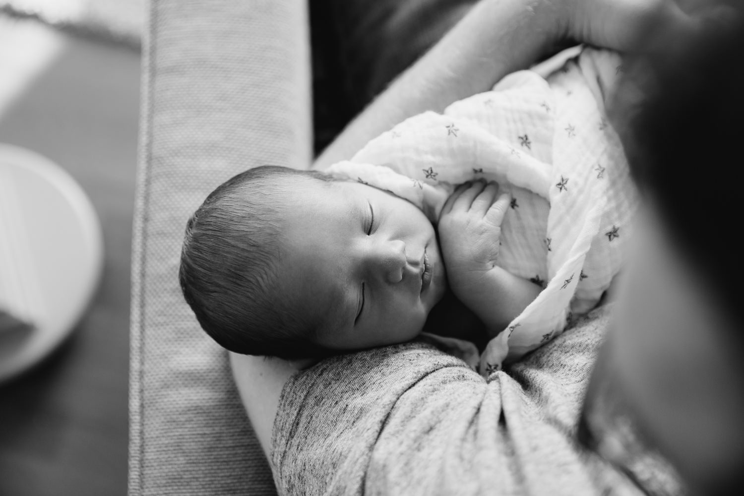 2 week old baby boy with dark hair swaddled and sleeping in dad's arms, father sitting in chair - York Region In-Home Photography