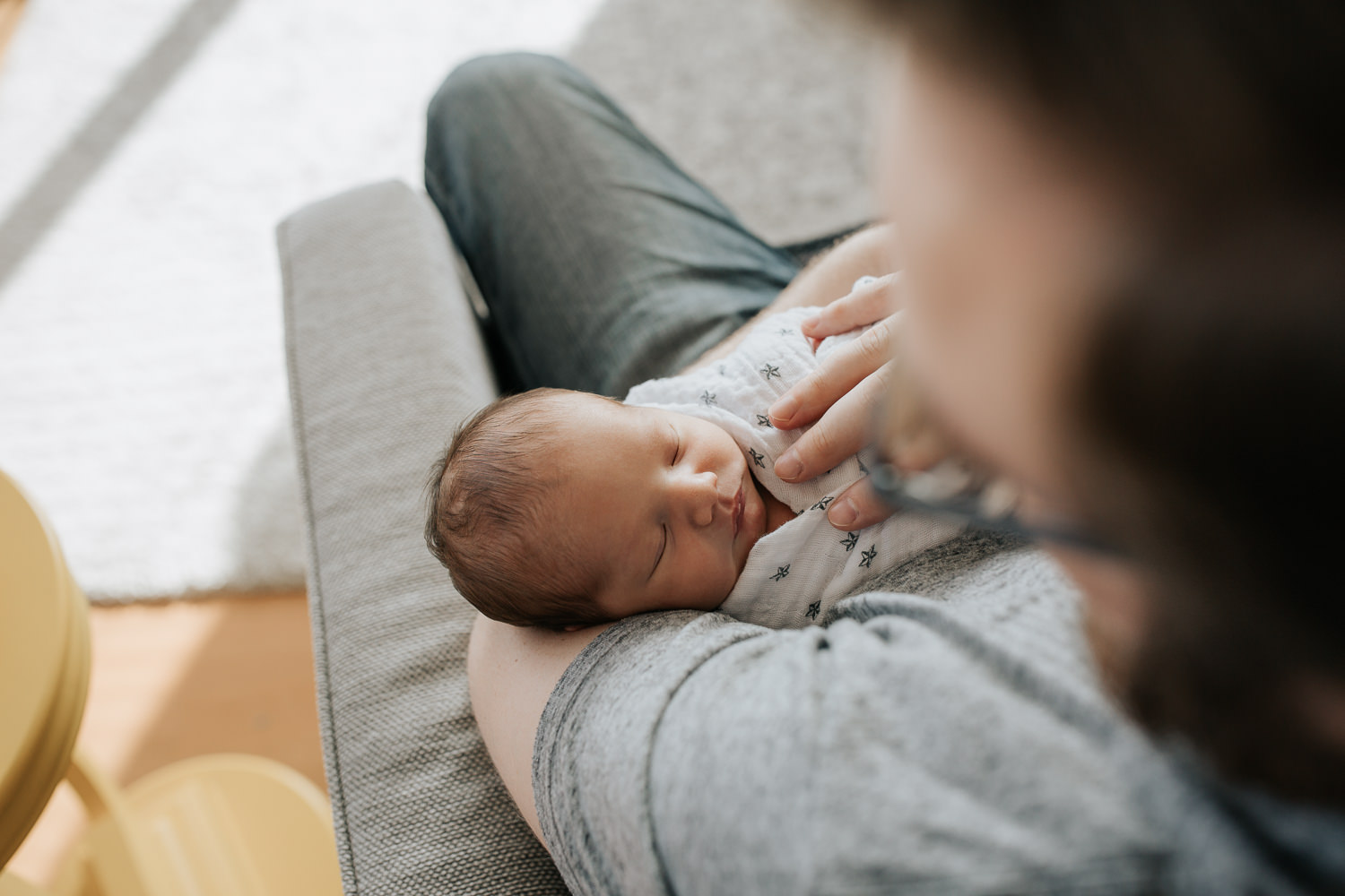 2 week old baby boy with dark hair swaddled and sleeping in dad's arms, father sitting in chair - GTA In-Home Photography