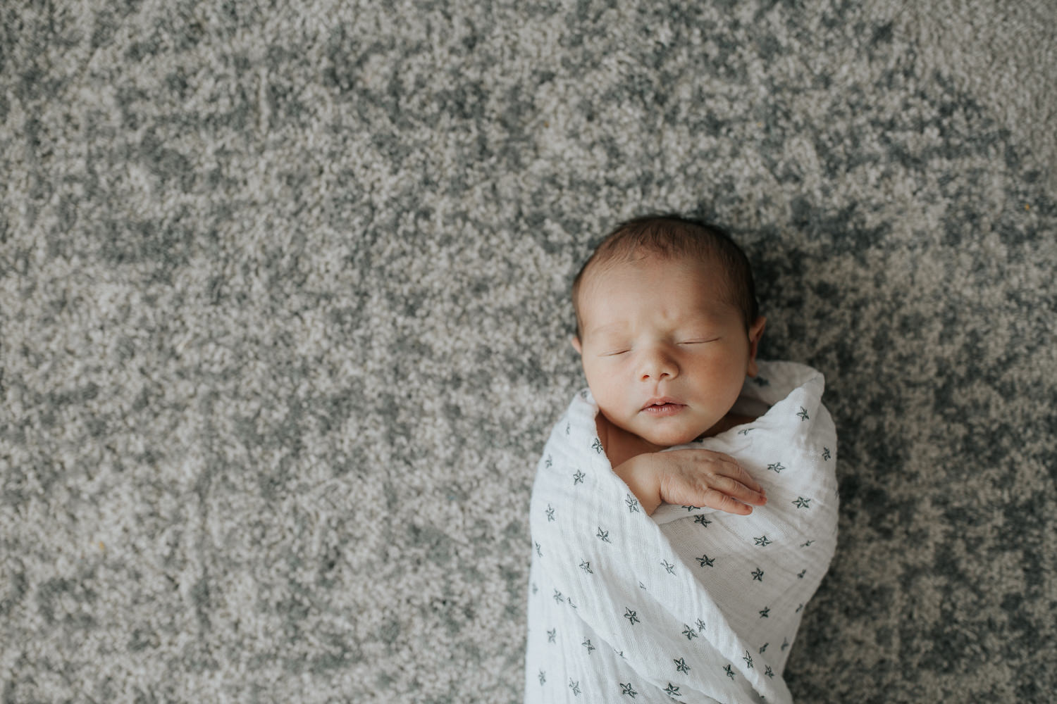 2 week old baby boy with dark hair and olive skin wrapped in swaddle with star on it, sleeping with hands near face - Barrie In-Home Photos