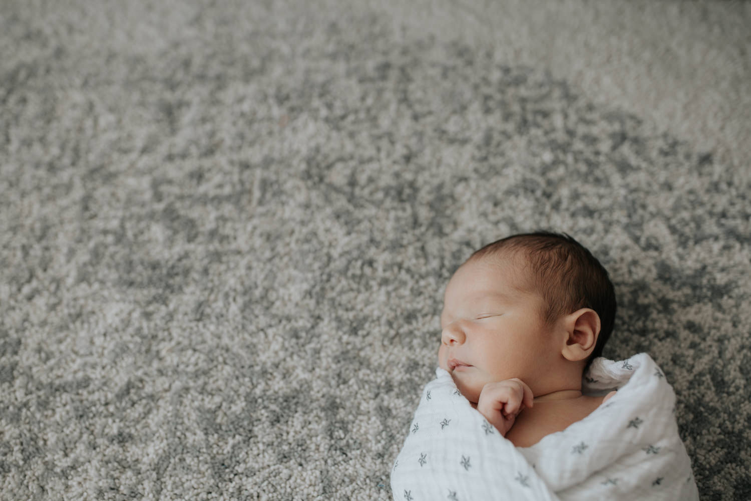 2 week old baby boy with dark hair and olive skin wrapped in swaddle with star on it, sleeping with hands near face - York Region In-Home Photos