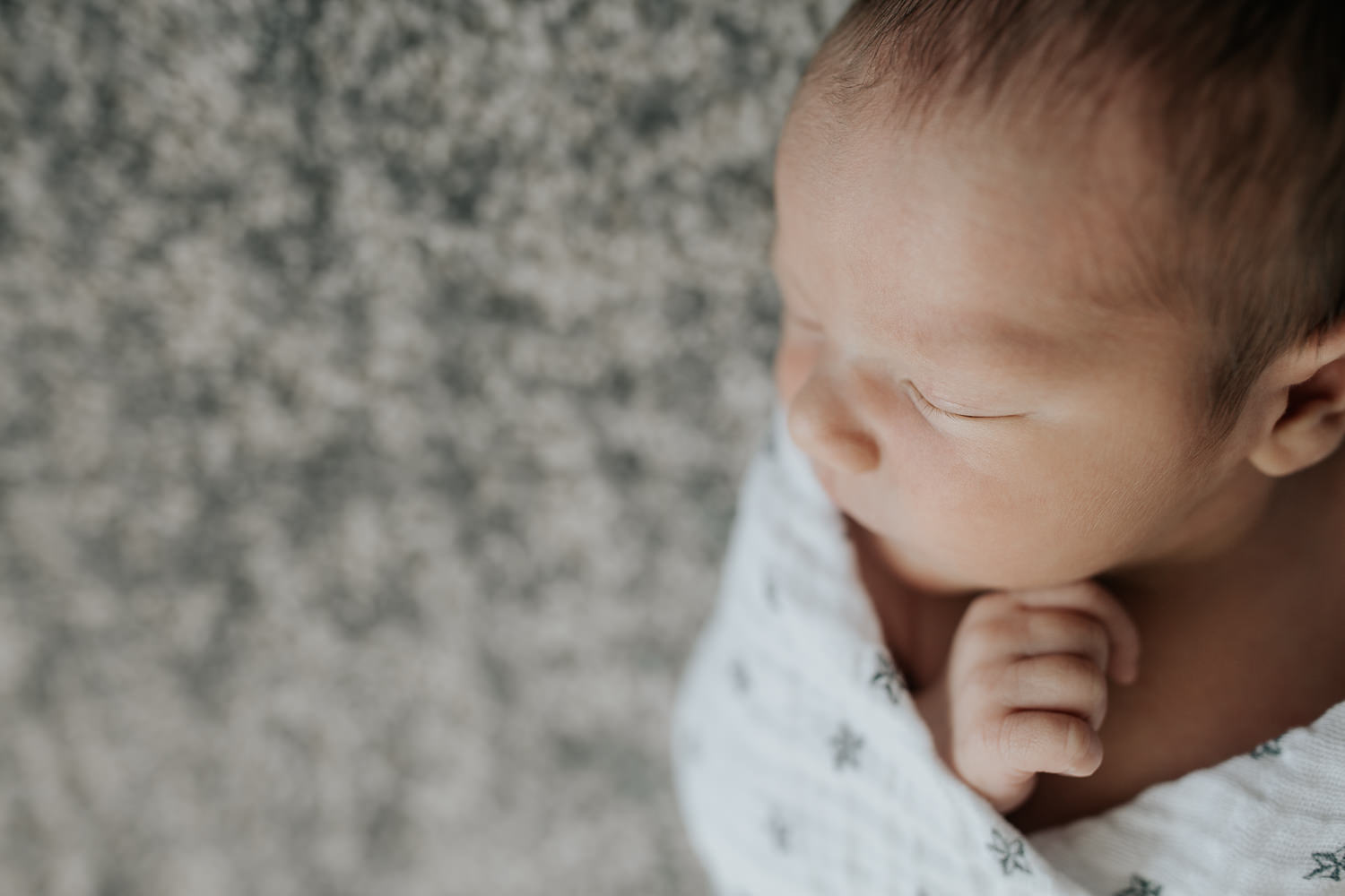 close up of 2 week old baby boy with dark hair and olive skin wrapped in swaddle with star on it, sleeping with hand near face - Markham Lifestyle Photos