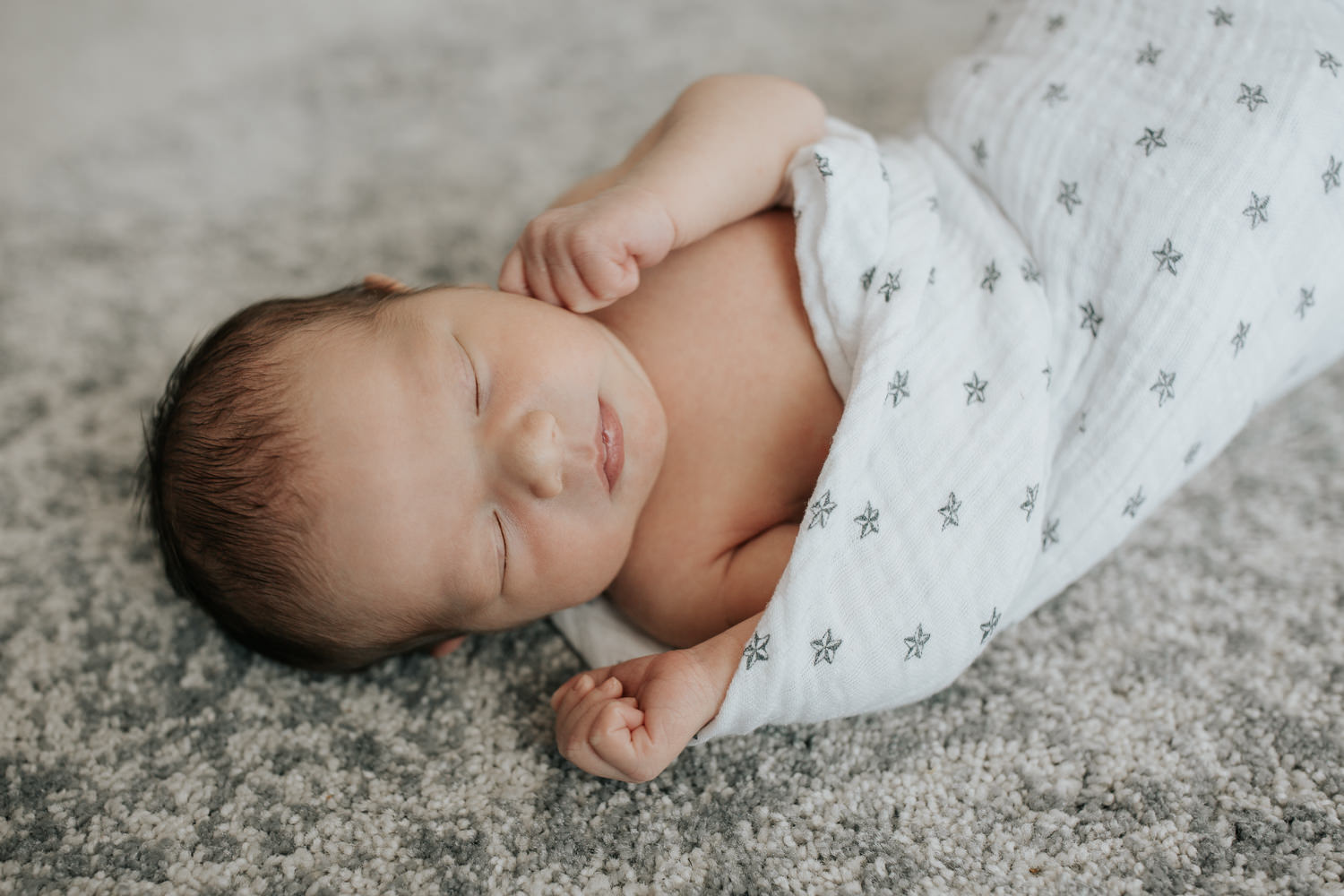 close up of 2 week old baby boy with dark hair and olive skin wrapped in swaddle with star on it, sleeping with hands near face - GTA Lifestyle Photos