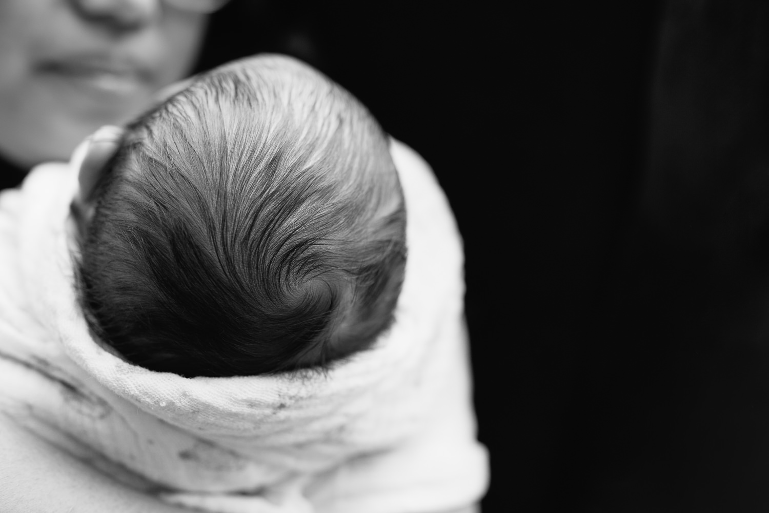 close up of 2 week old baby boy's swirl of dark hair on the top of his head while sleeping in mom's arms - GTA In-Home Photos