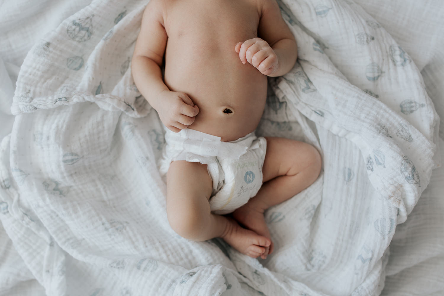 sleeping 2 week old baby boy in diaper lying on swaddle, hands resting on stomach, close up of torso and legs - Barrie Lifestyle Photos