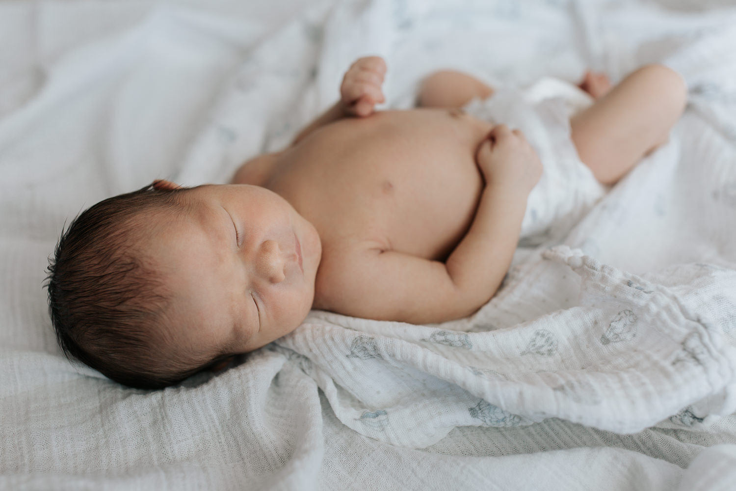 sleeping 2 week old baby boy in diaper lying on swaddle, head to side, hands resting on stomach - Markham Lifestyle Photography