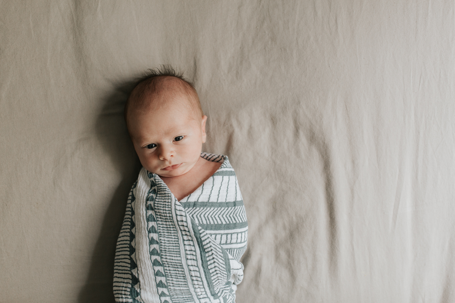 2 week old baby boy in geometric blue and white swaddle awake lying on bed - Stouffville Lifestyle Photos