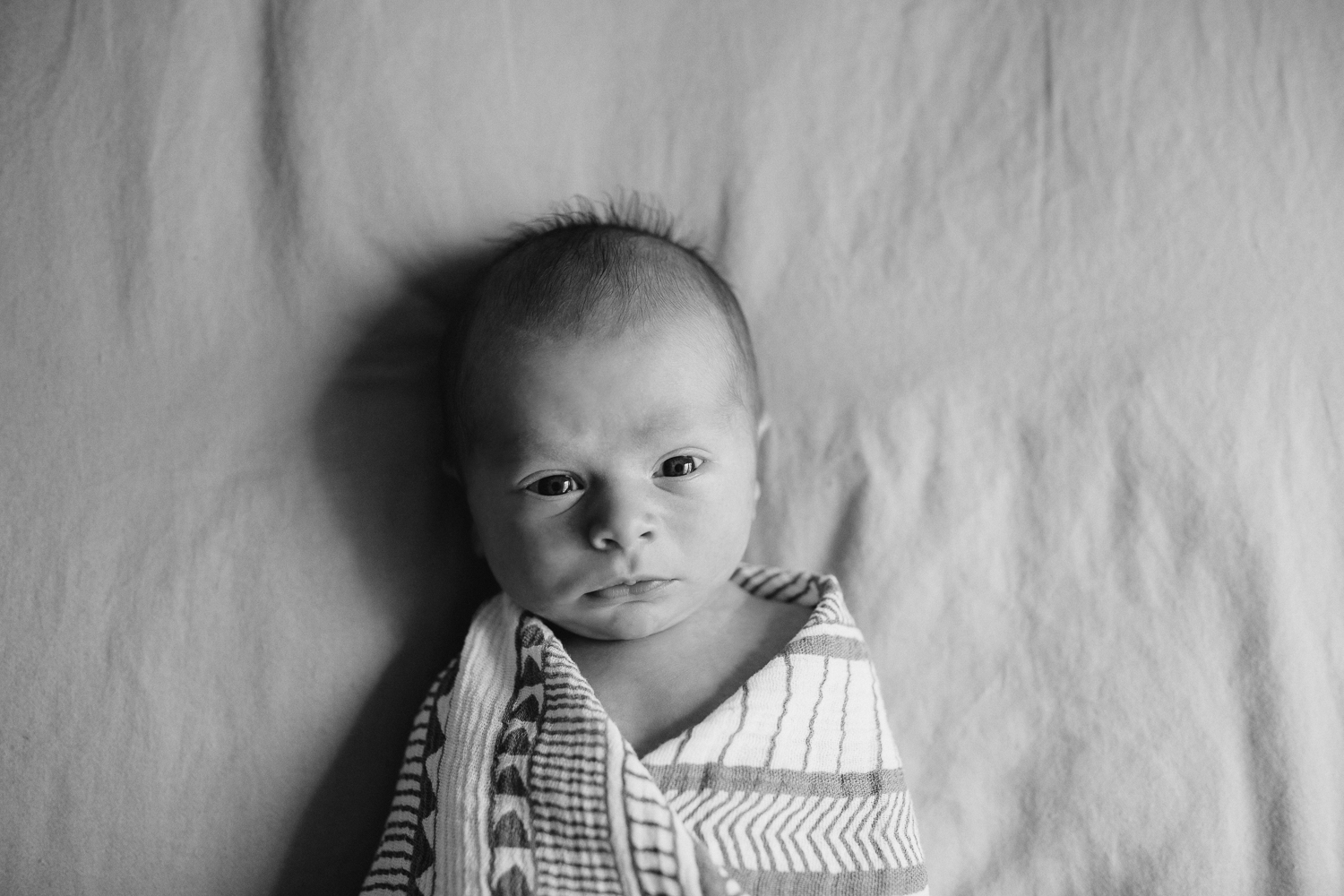 2 week old baby boy in geometric swaddle awake lying on bed looking at camera - GTA Lifestyle Photos