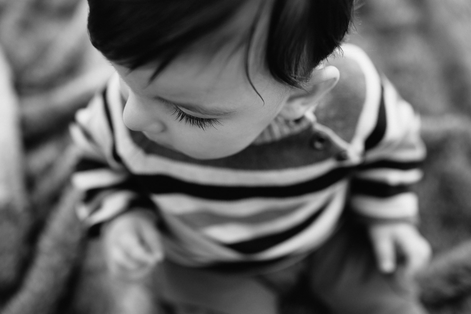 1 year old boy with dark hair and eyes wearing striped sweater sitting on blanket in outdoor path, close up of eyelashes - Stouffville Golden Hour Photos