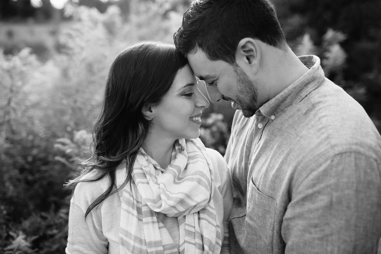 couple standing in field at sunset, sun setting behind them, husband's arms around wife's waist, couple face-to-face, nose and foreheads touch, smiling -​​​​​​​ York Region Lifestyle Photography