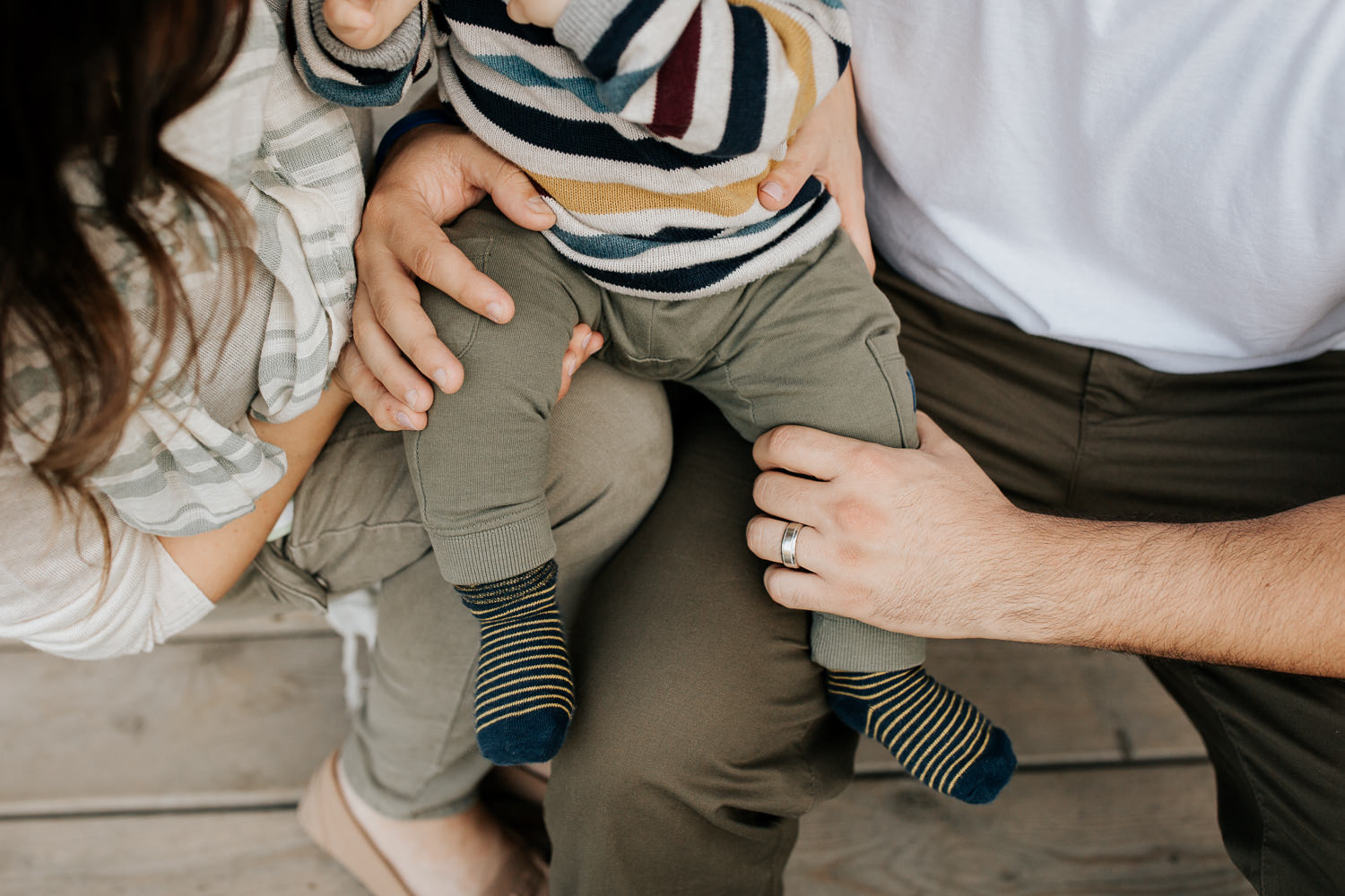 family of 3 sitting on front porch steps of historic log cabin, son on parent's laps, close up of mom and dad's hands on child - Markham Outdoor Photography