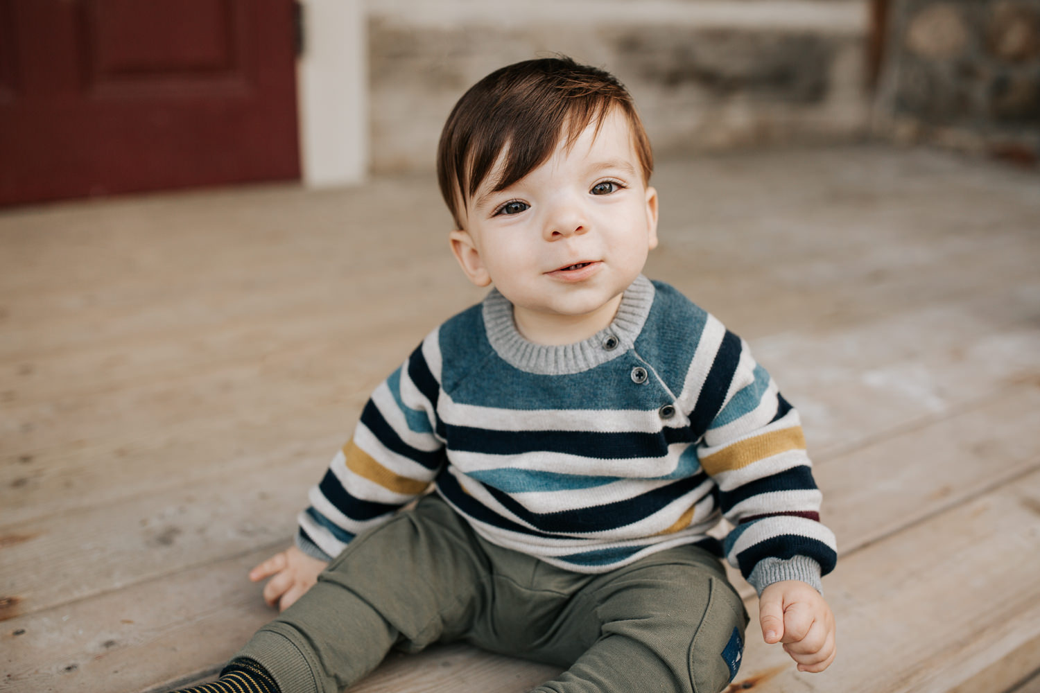 1 year old baby boy with brown hair and eyes in striped sweater sitting on front porch, looking at camera - Newmarket Outdoor Photography