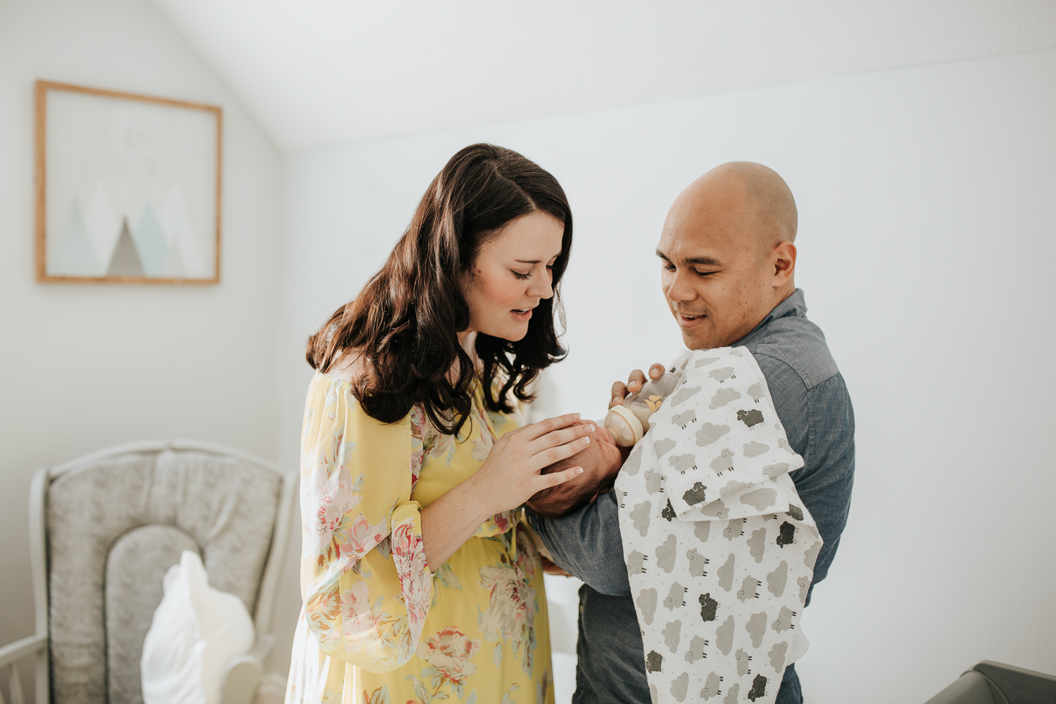 new parents standing in nursery, dad feeding 3 week old baby boy a bottle as mom stands next to them, hand on son's head - Newmarket Lifestyle Photography