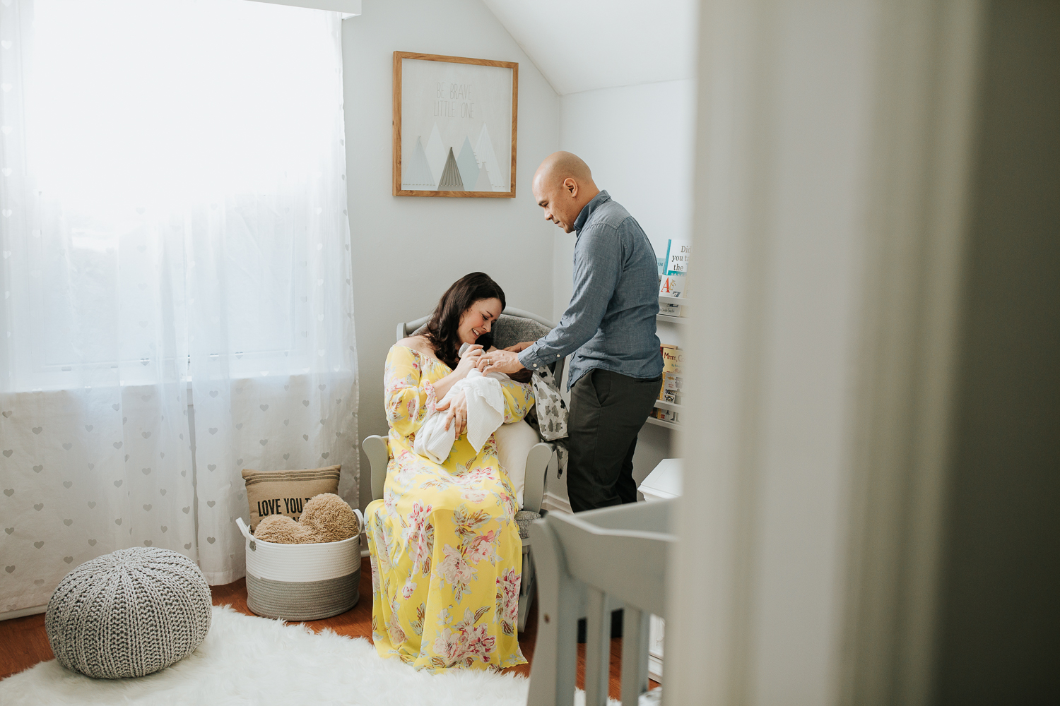 new mom in yellow dress sitting in nursery rocker feeding 3 week old baby boy his bottle, father standing next to chair holding son's hand - GTA Lifestyle Photography